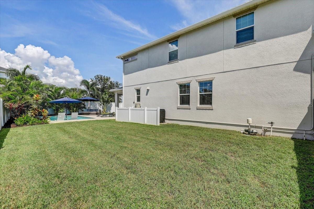 Two-story stucco home beside a lawn, with a fenced pool, patio umbrellas, and tropical landscaping.