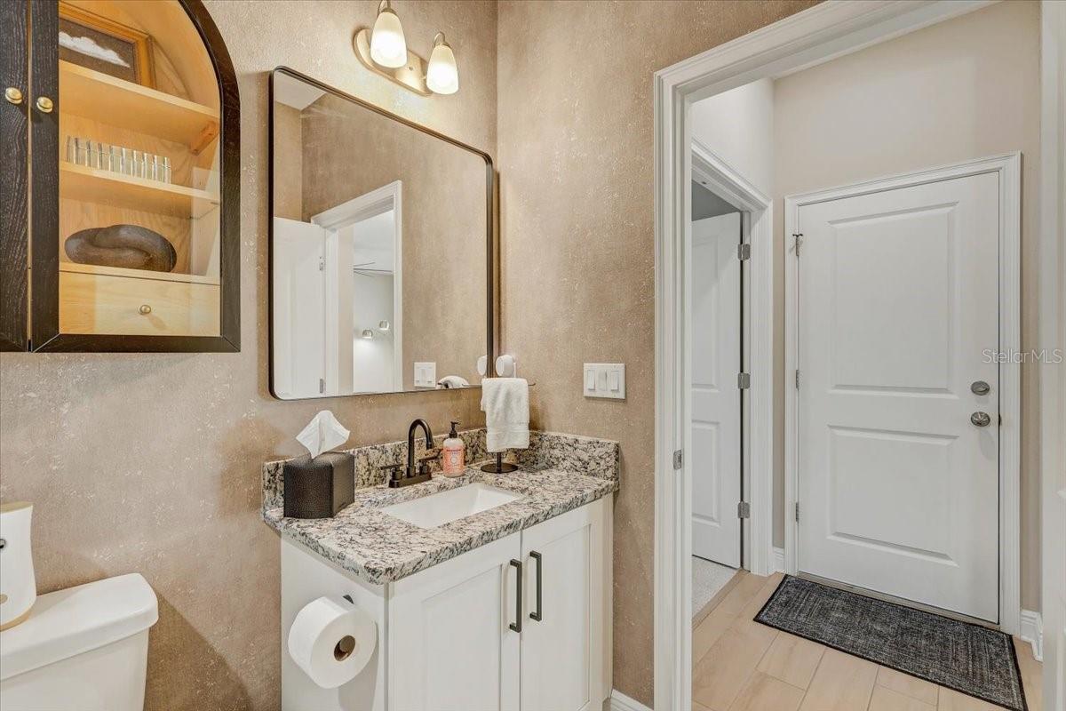 Bathroom with a granite vanity, mirrored cabinet, toilet, and white paneled door.