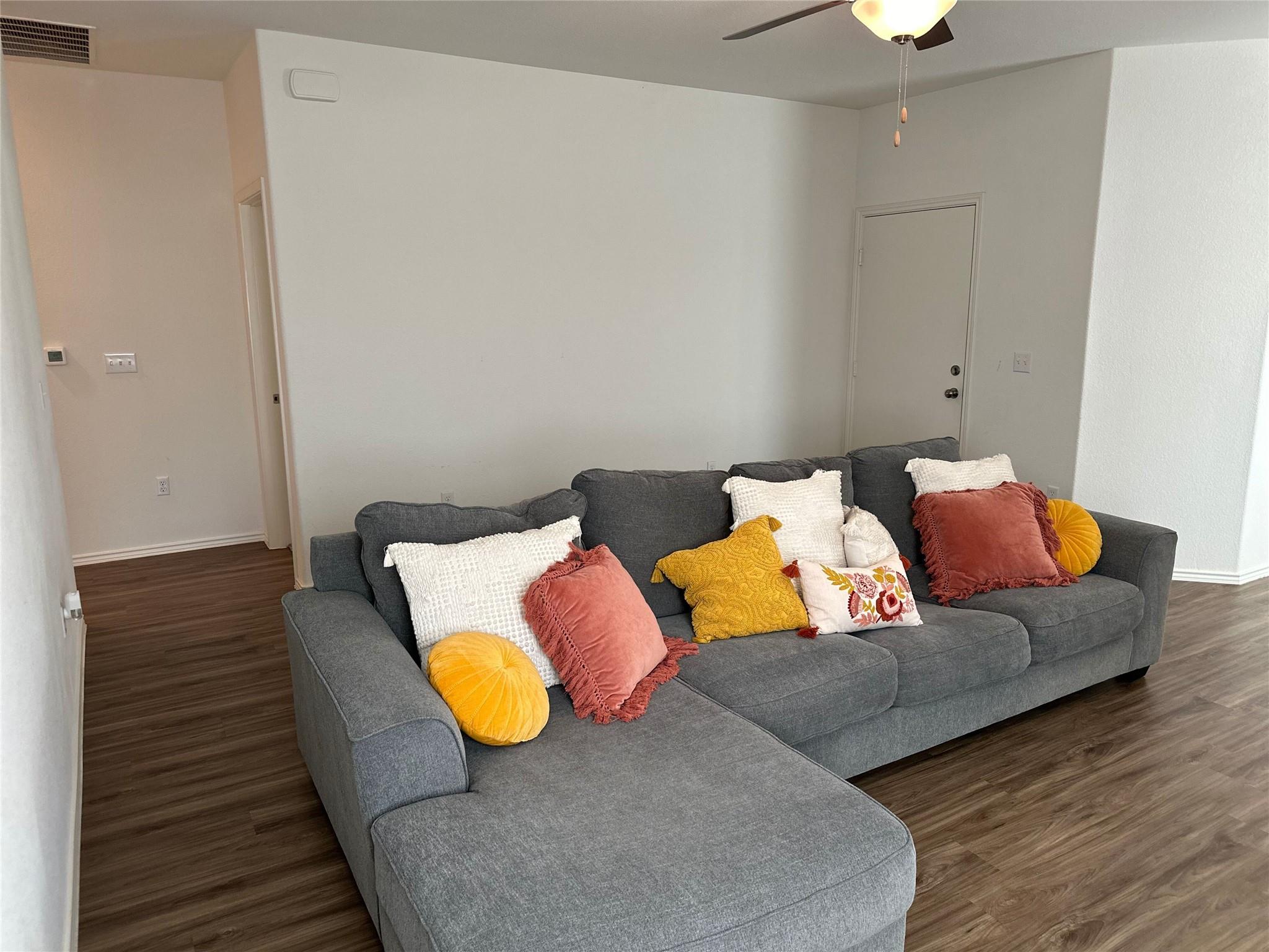 Living room with a gray sectional sofa and colorful accent pillows on dark wood flooring.