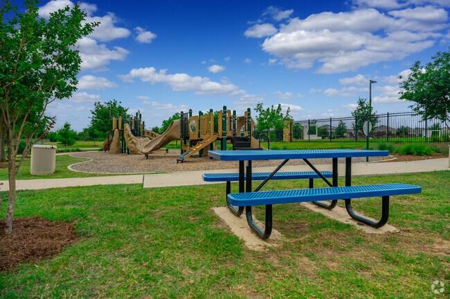Community playground with a wooden play structure, blue picnic table, and fenced recreation area.