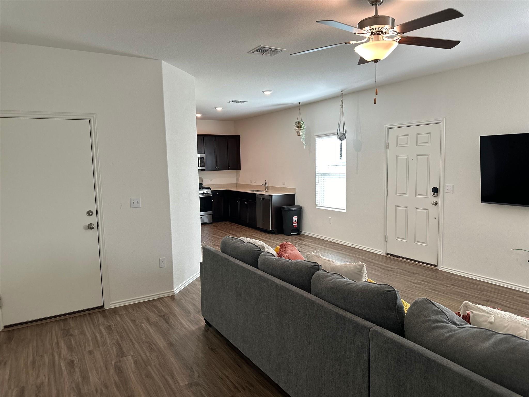 Open-plan living room and kitchen with a gray sectional, dark cabinets, and wood-look floors.