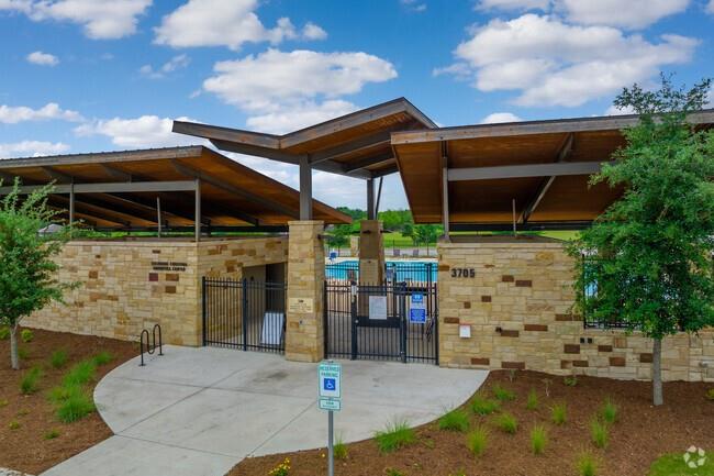Gated swimming pool entrance with tan stone walls and a broad modern wood canopy.