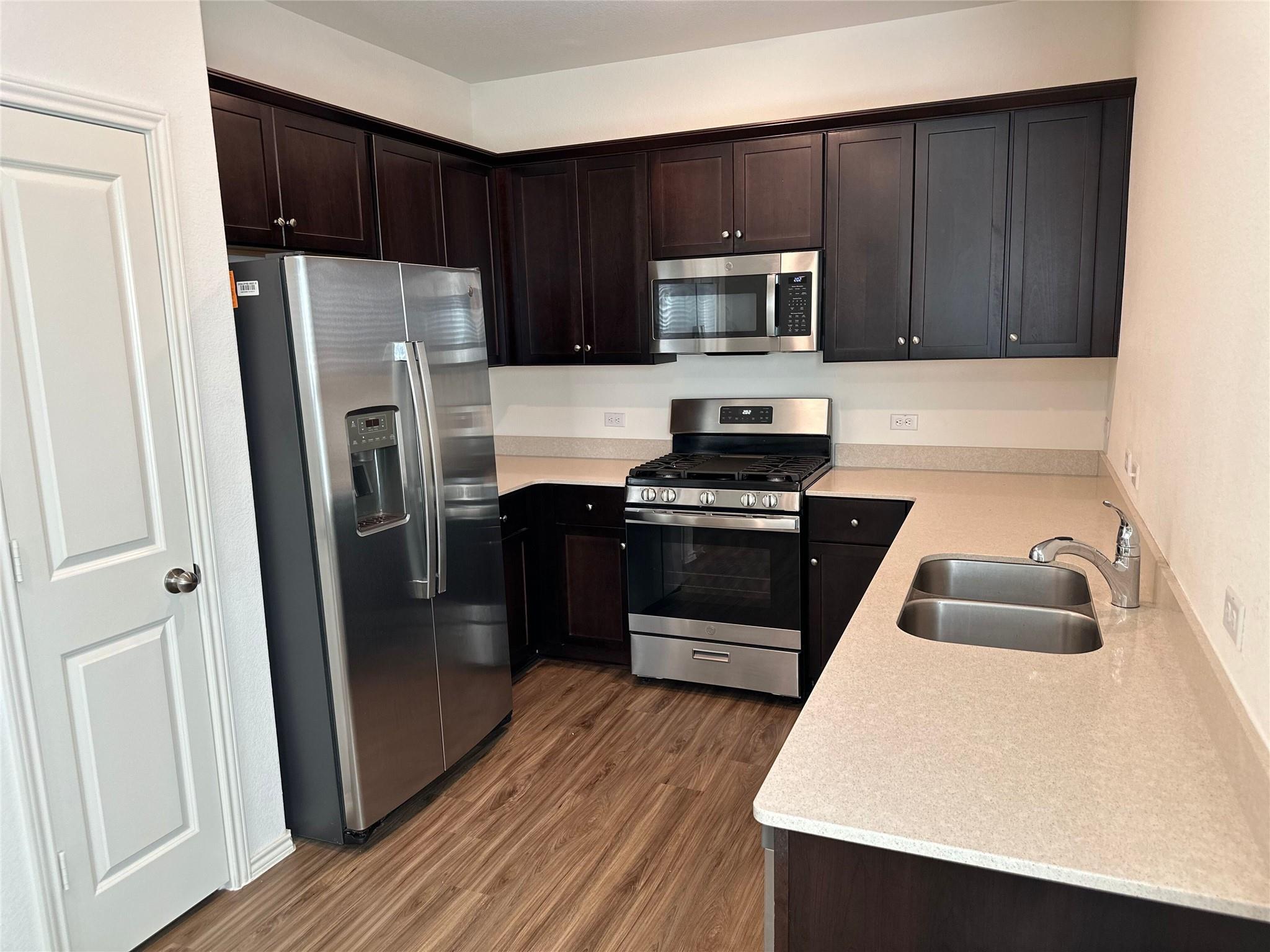 Kitchen with dark cabinets, stainless steel appliances, gas range, and double-basin sink.