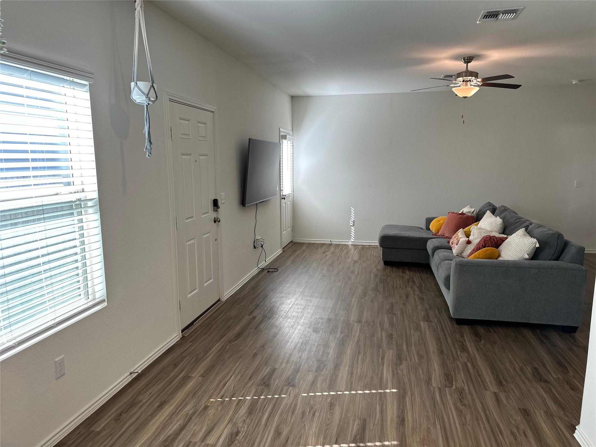 Living room with a gray sectional sofa, wall-mounted television, and dark wood-look flooring.