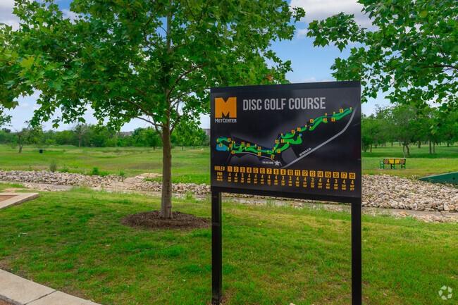 Disc golf course sign with a course map beside a grassy, tree-lined course.