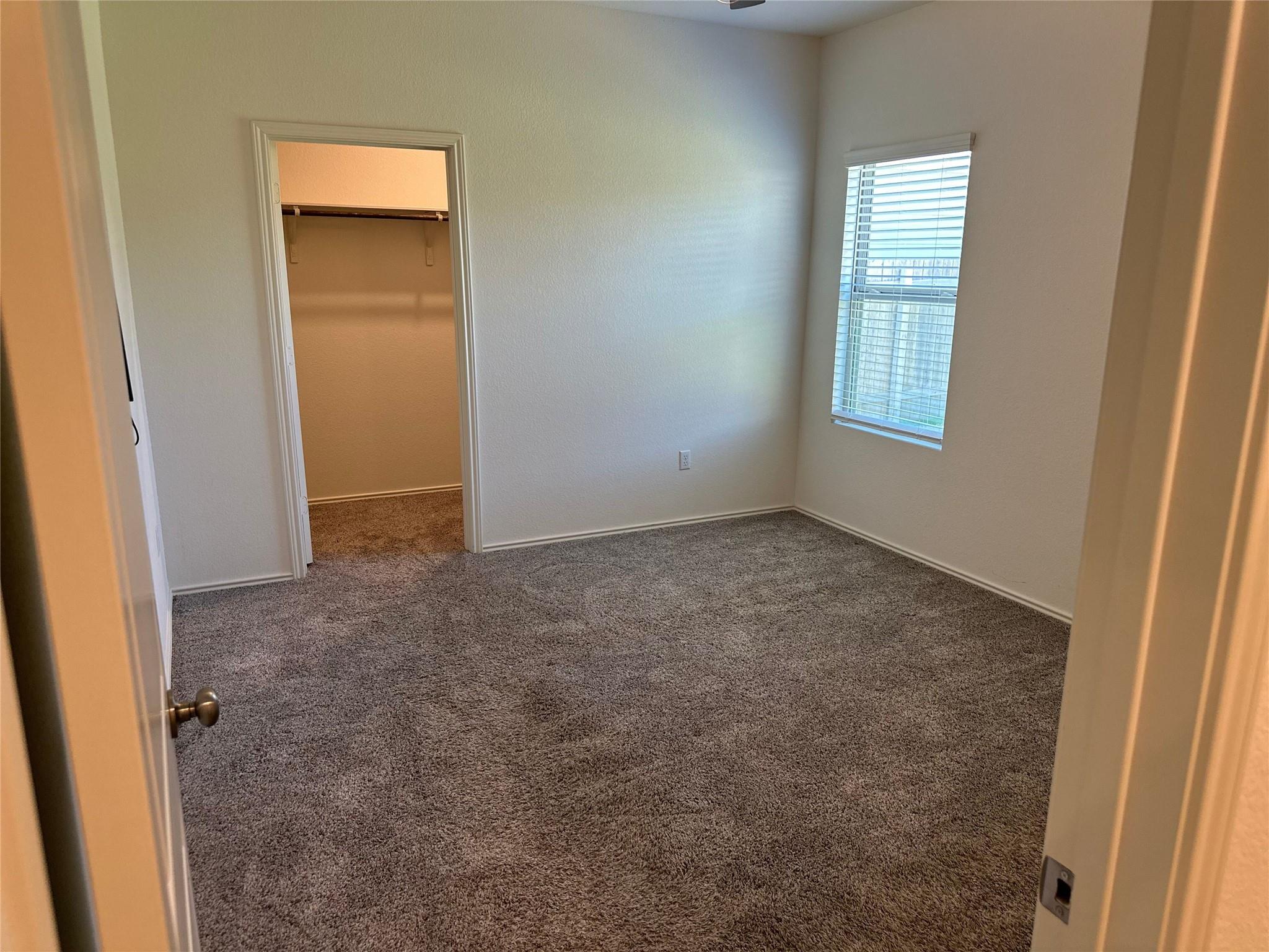 Vacant bedroom with carpet, a window with blinds, and an open closet.