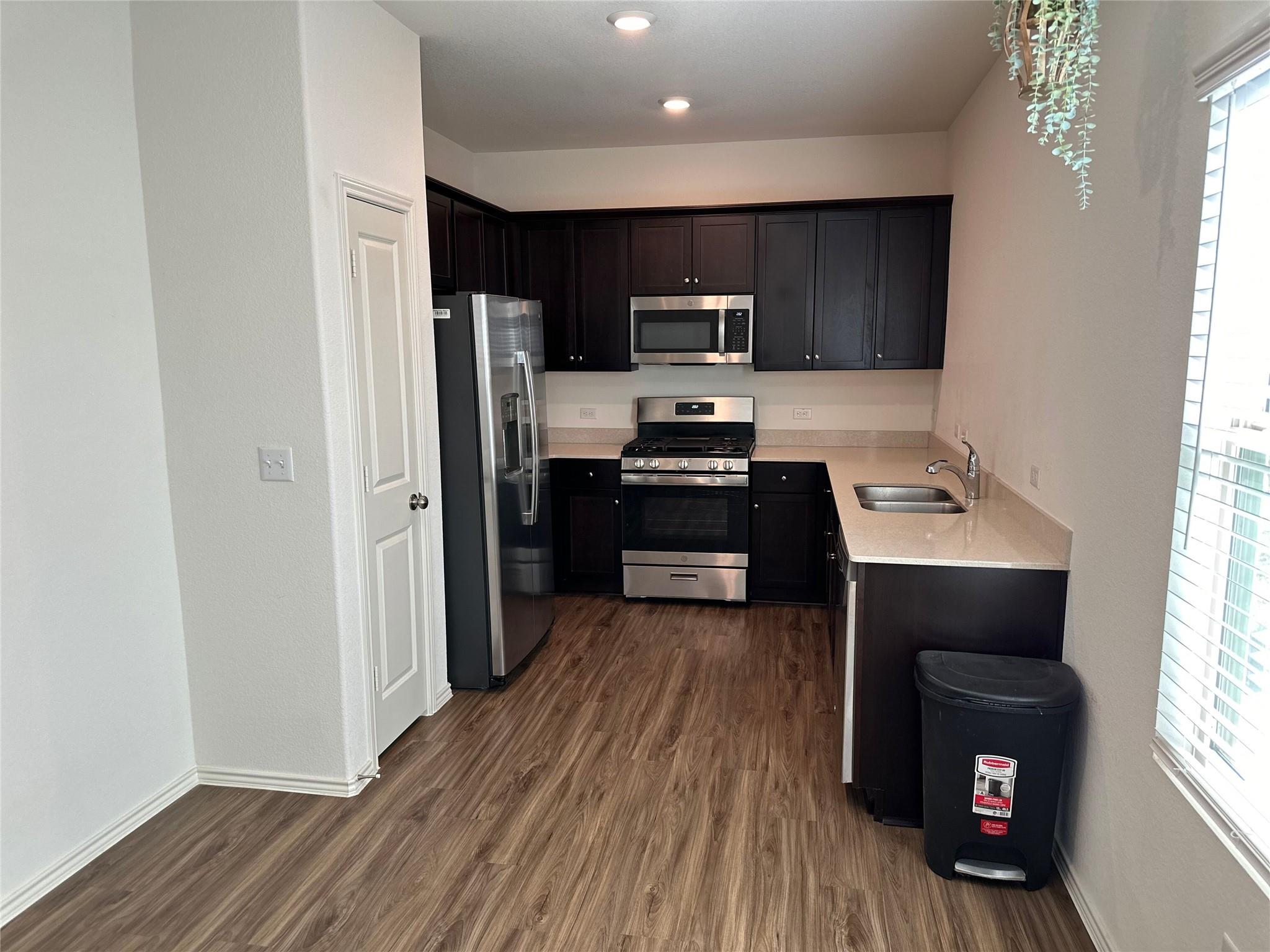 Kitchen with dark cabinets, stainless steel appliances, and wood-look flooring.