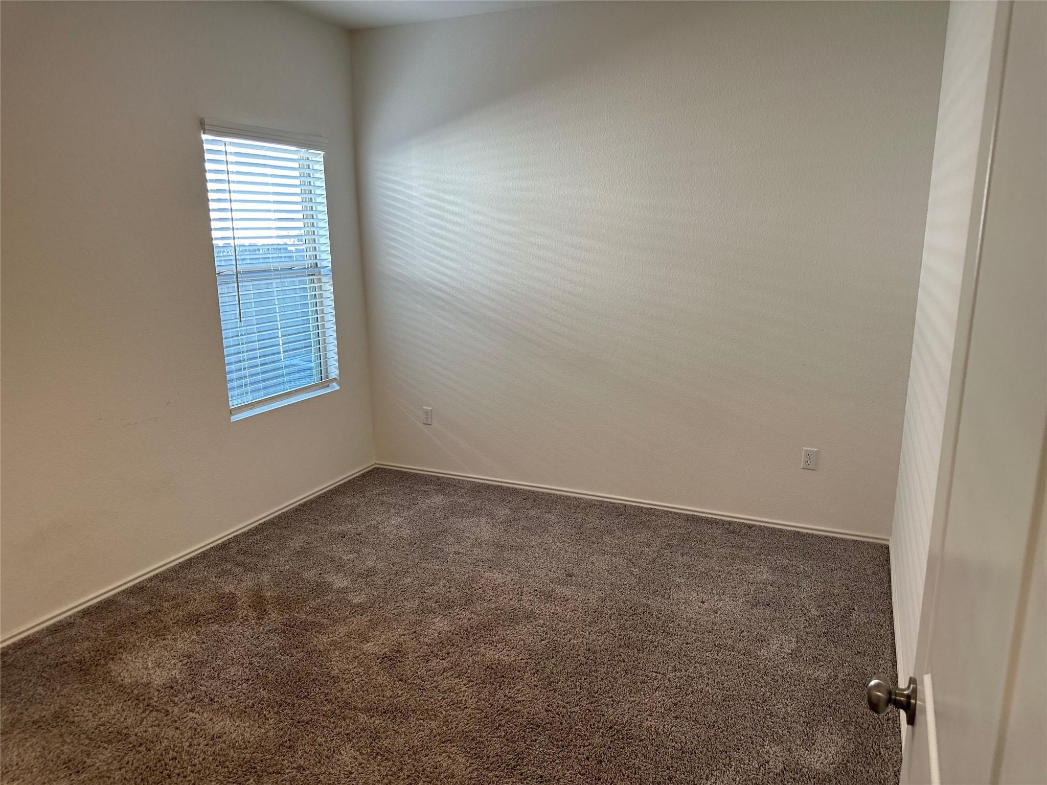 Empty bedroom with brown carpeting and a window with horizontal blinds.
