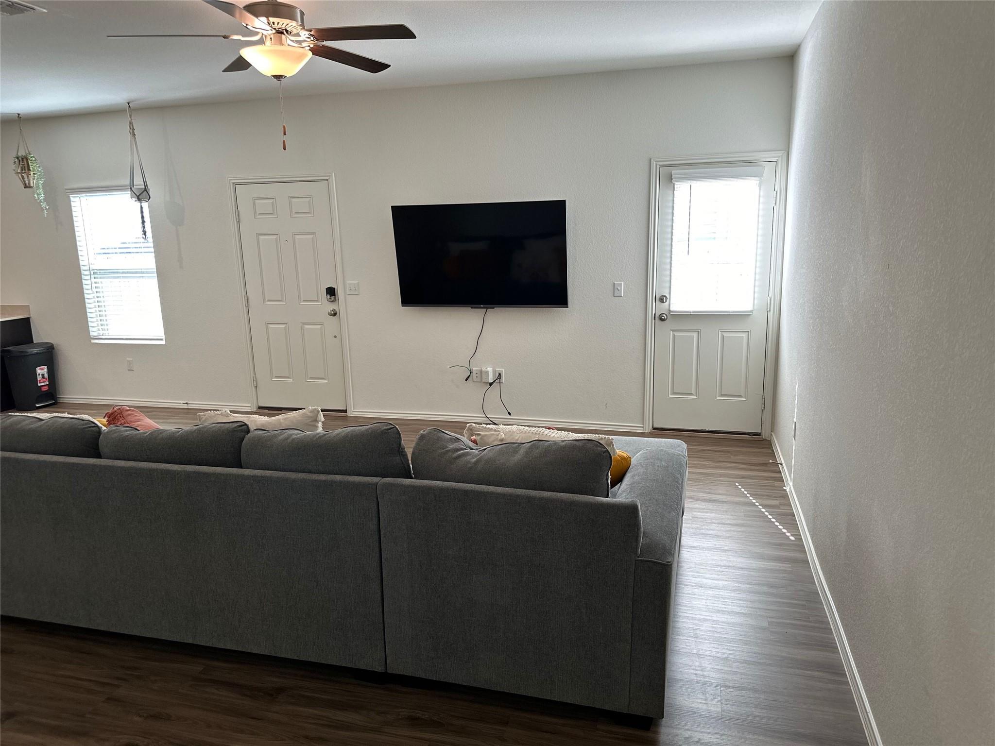 Living room with a gray sectional facing a wall-mounted TV, two doors, and wood-look flooring.