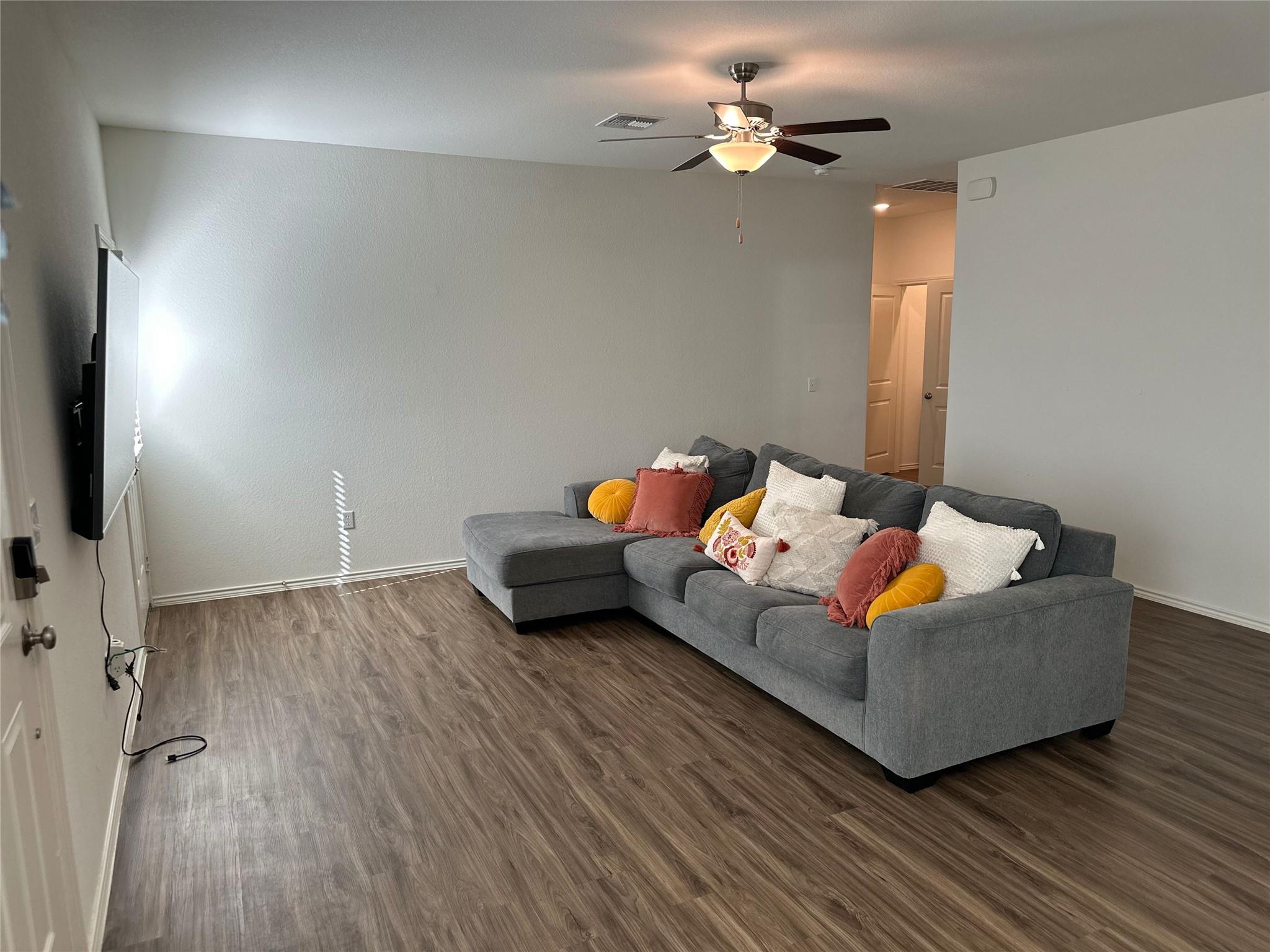 Living room with a gray sectional, colorful pillows, wood-look floors, and a ceiling fan.