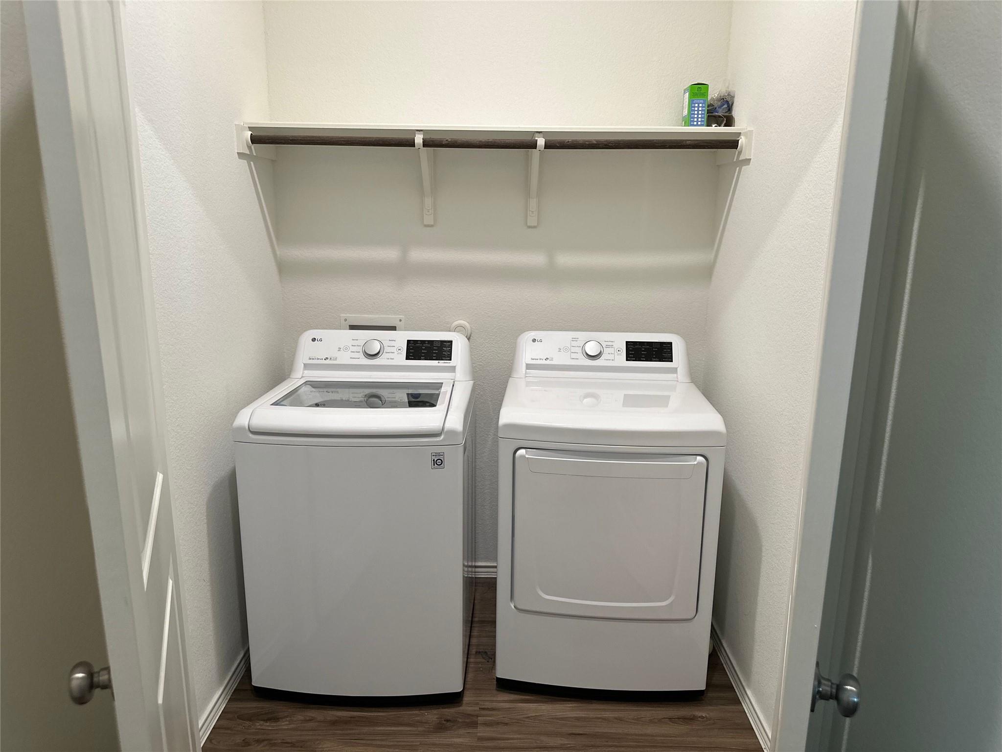 Laundry room with a white washer and dryer beneath a long wall-mounted shelf.
