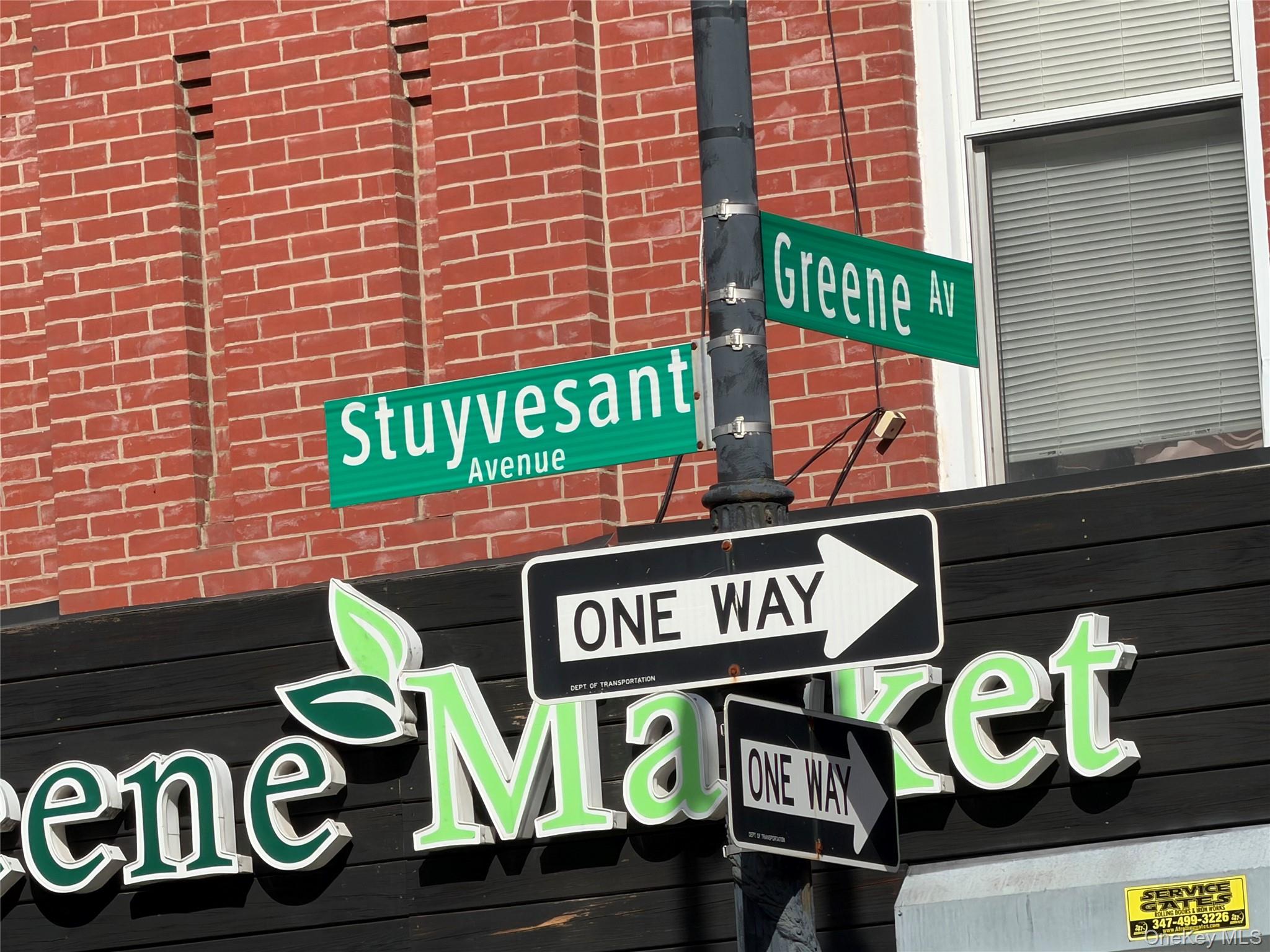 Greene Avenue and Stuyvesant Avenue street signs above one-way signs and a red brick building.