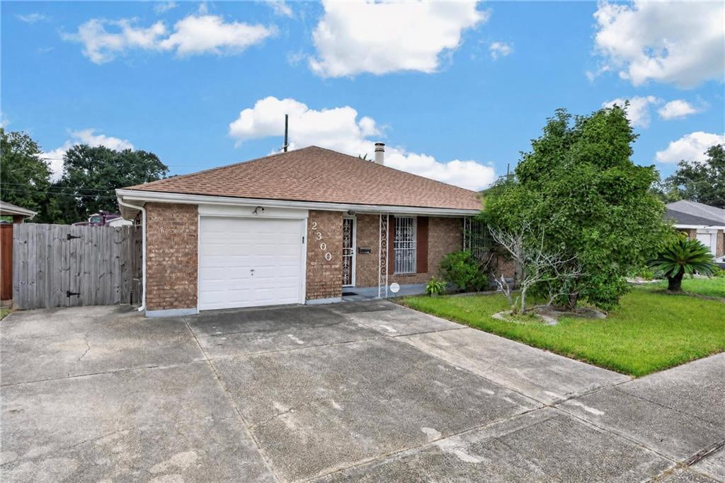 Single-story brick house with a white garage, broad driveway, and mature tree in the front yard.