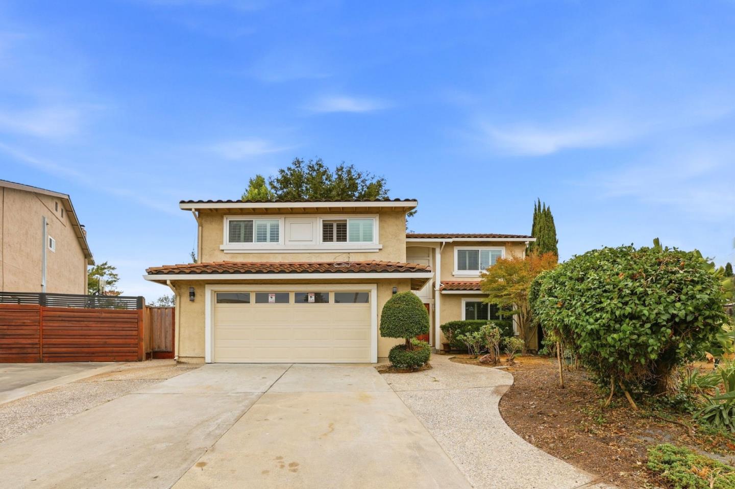 Two-story beige stucco home with a tile roof, double garage, and landscaped front yard.