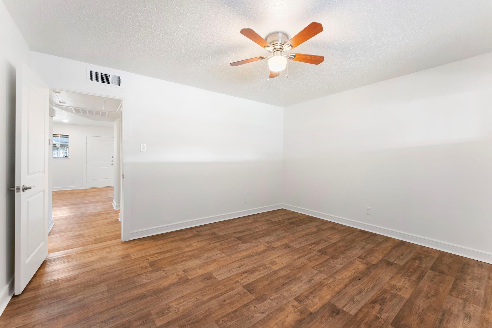 Empty room with wood-look flooring and a ceiling fan, viewed through an open doorway.