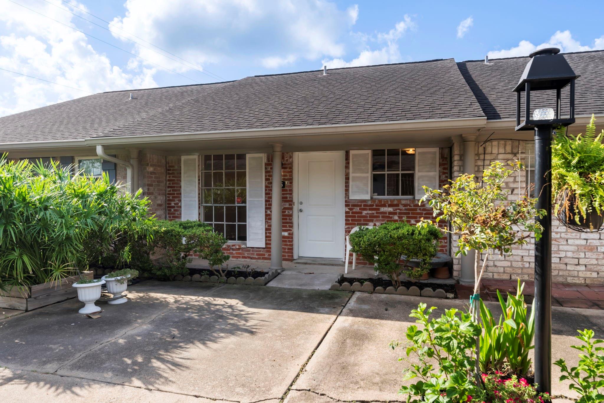 Brick home exterior with a covered entry, white door, shuttered windows, and landscaped front walkway.