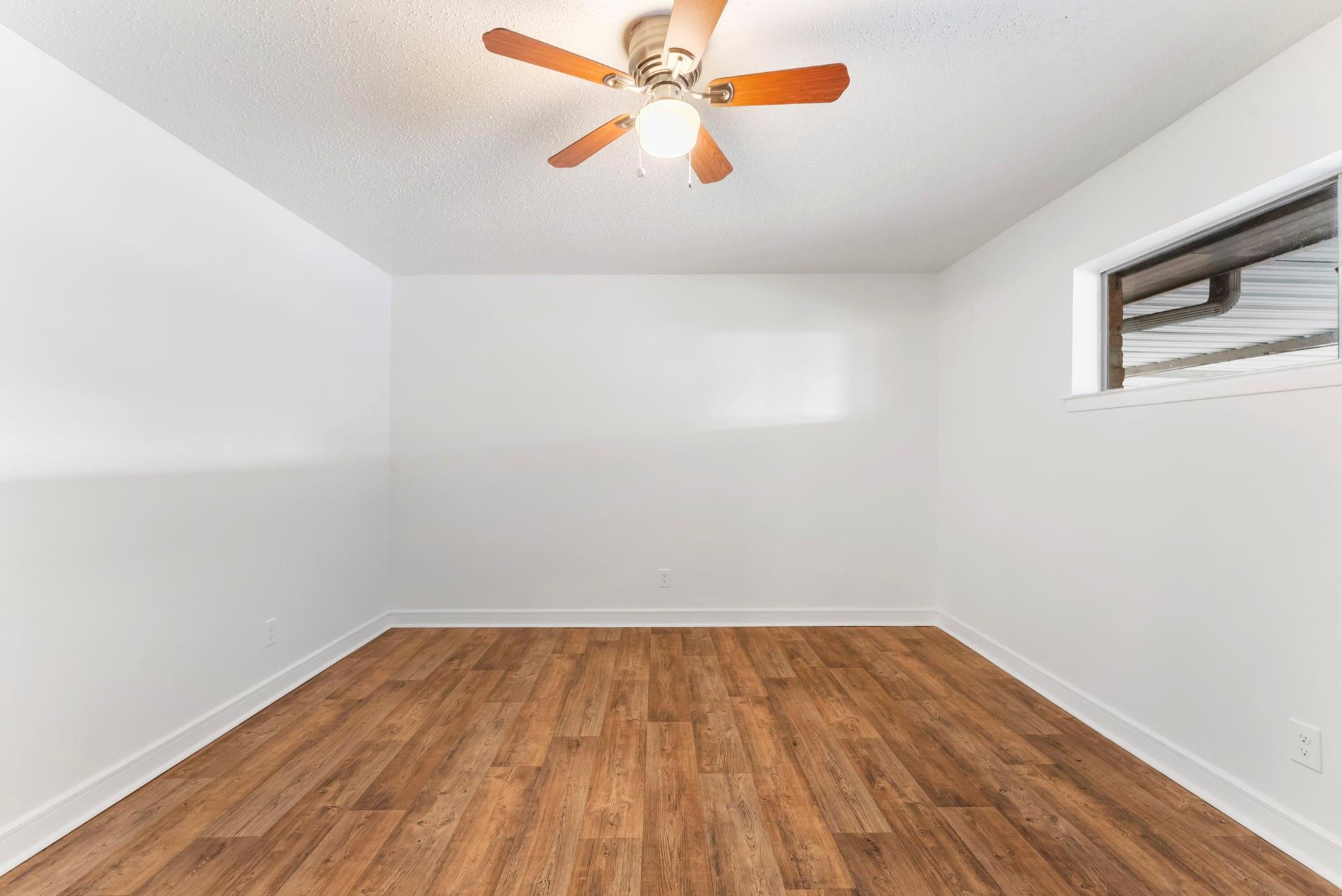 Empty room with wood-look flooring, a ceiling fan, and a small high window.