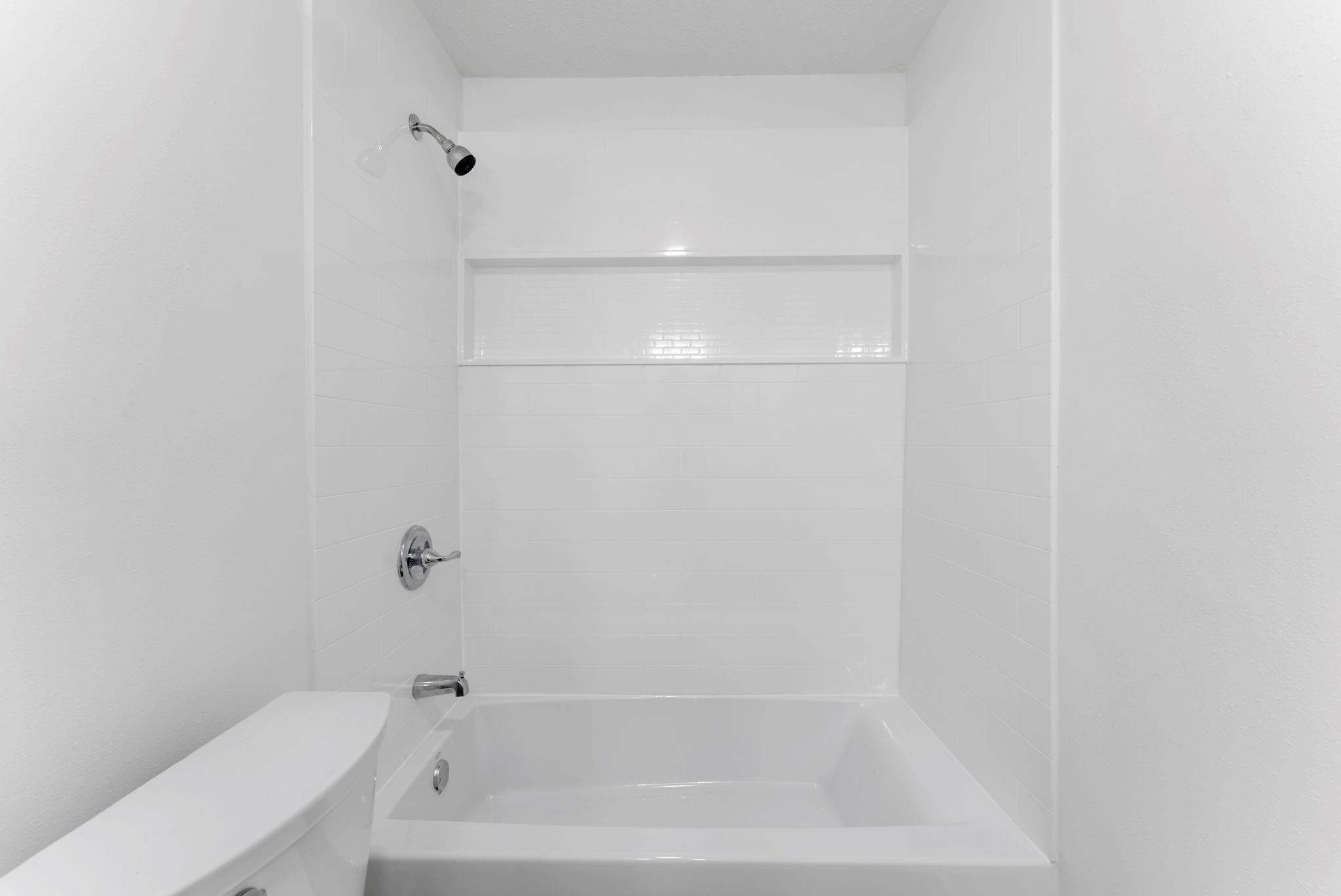White bathtub and shower with tiled walls and a recessed niche.
