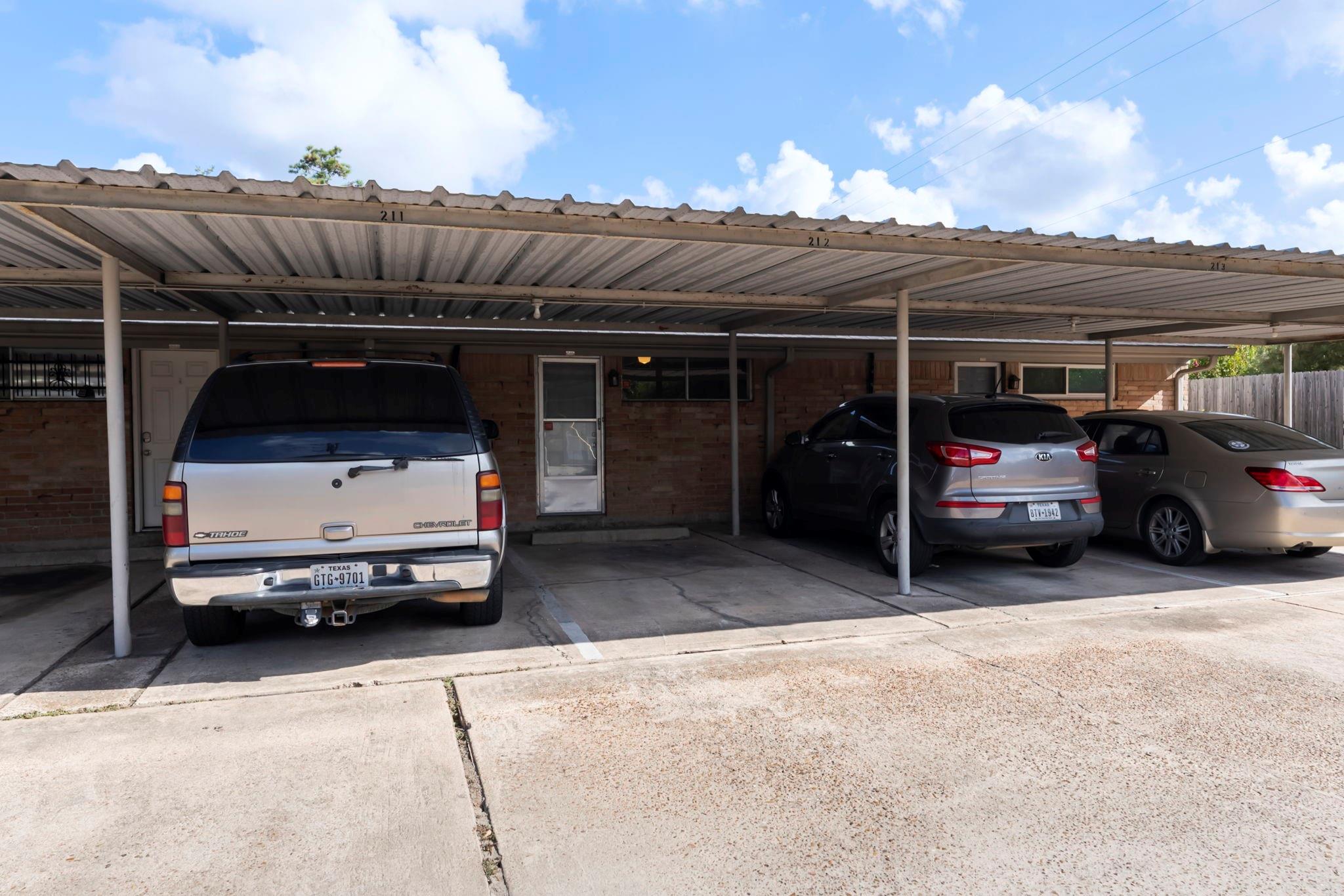 Brick residential building with a covered carport and three parked vehicles.