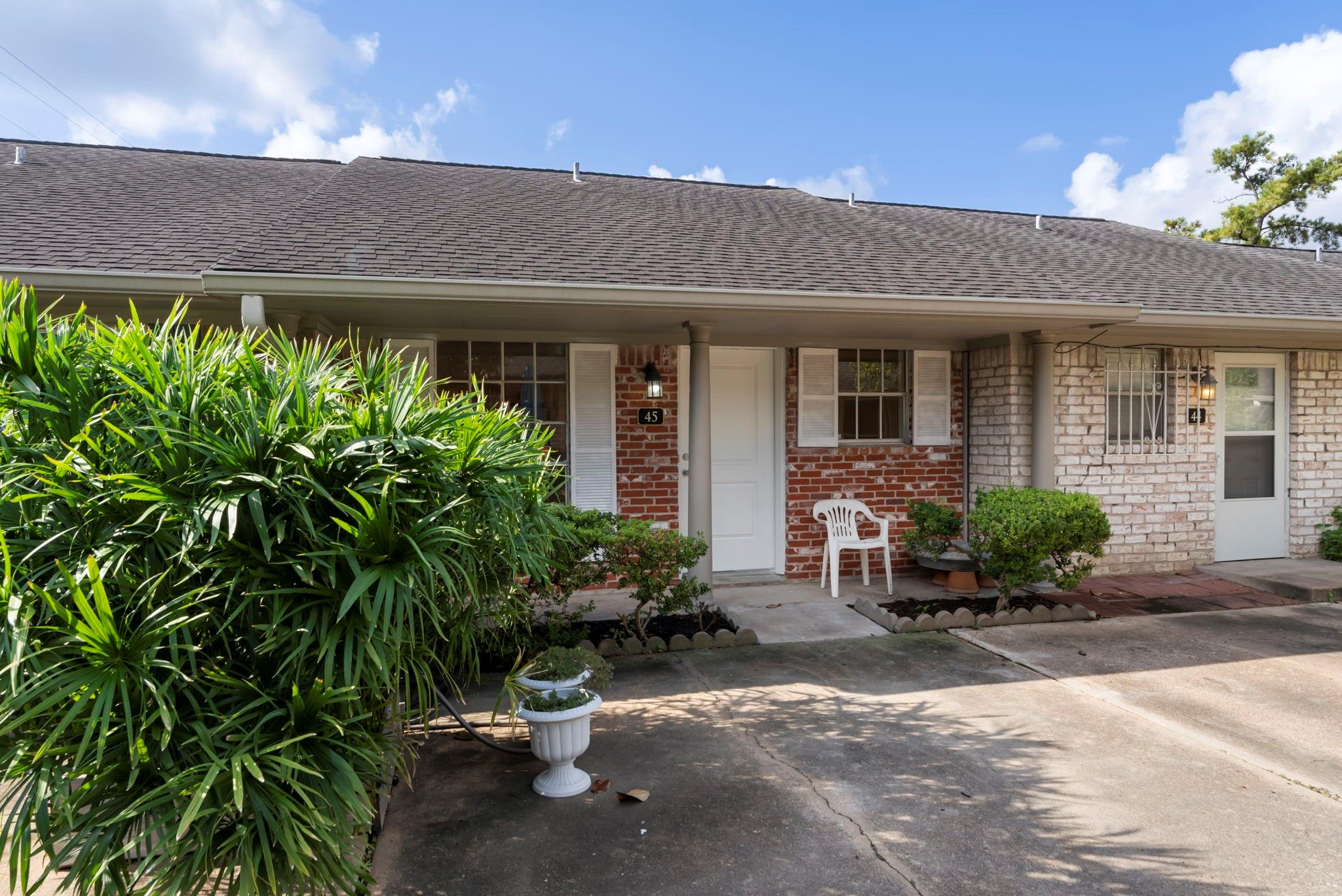 Brick home unit 45 with a covered entry, white front door, and dense shrubs.