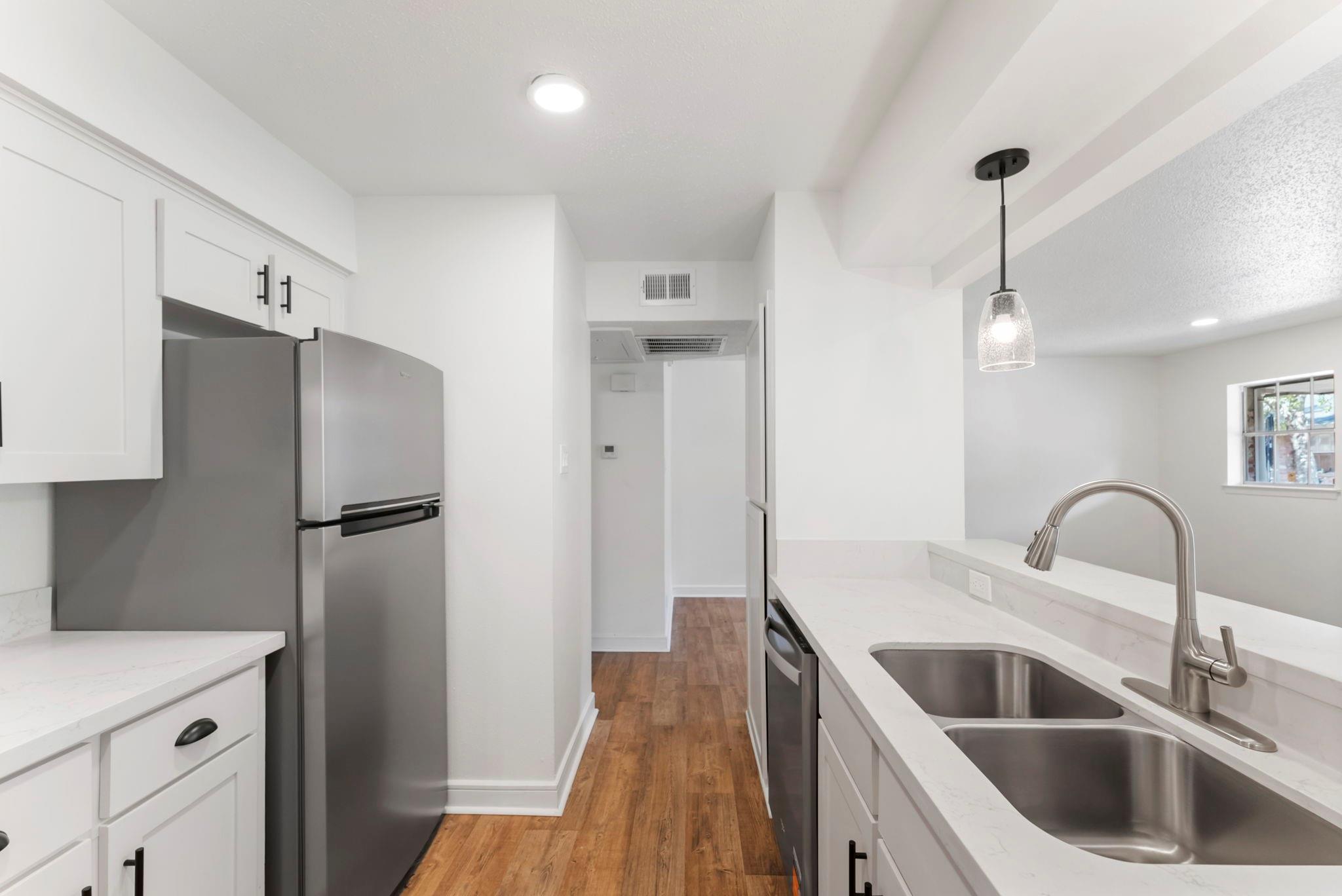 Kitchen with white cabinets, stainless steel appliances, a double sink, and warm wood flooring.