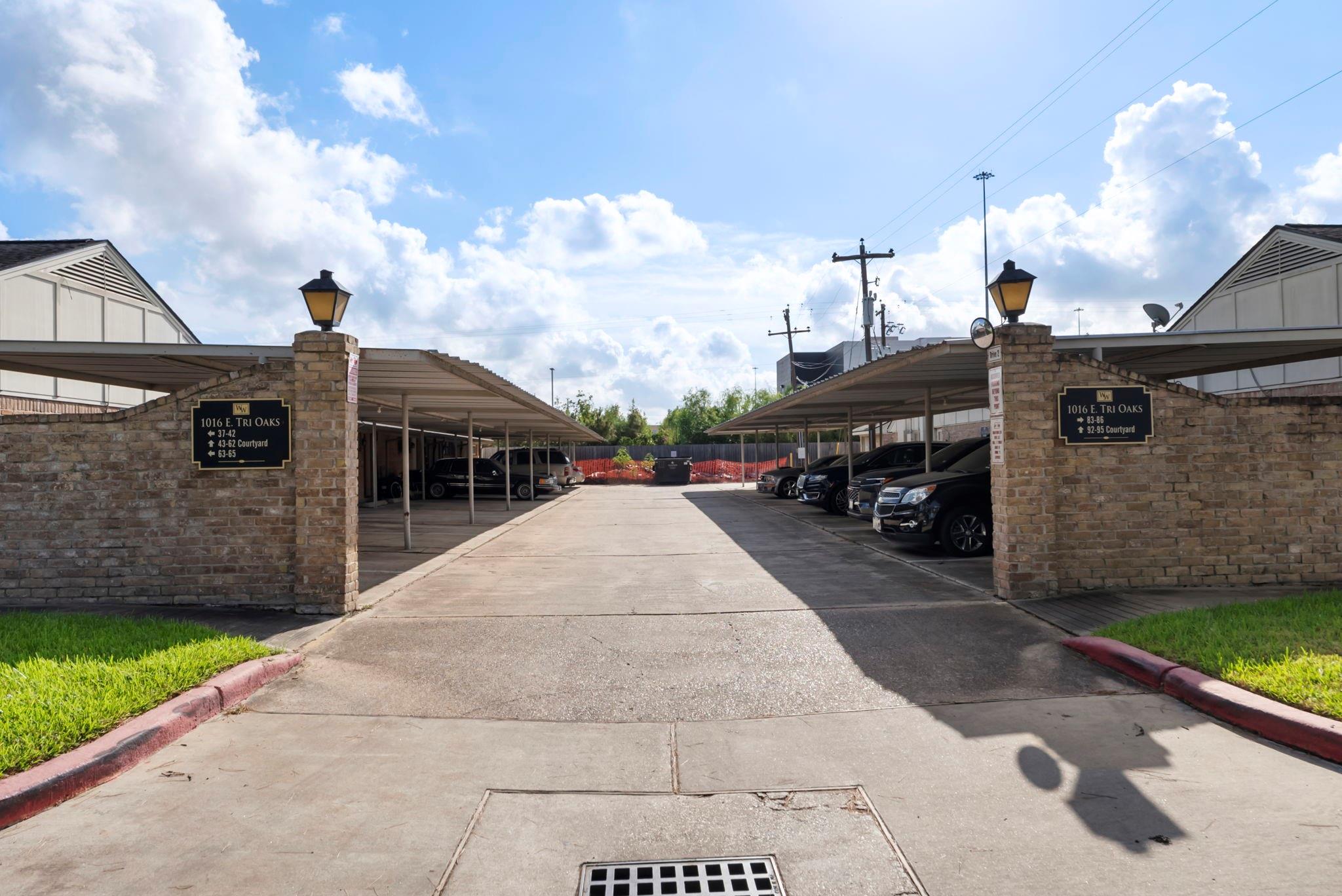 Apartment complex entrance with brick sign pillars, covered carports, and a central driveway.