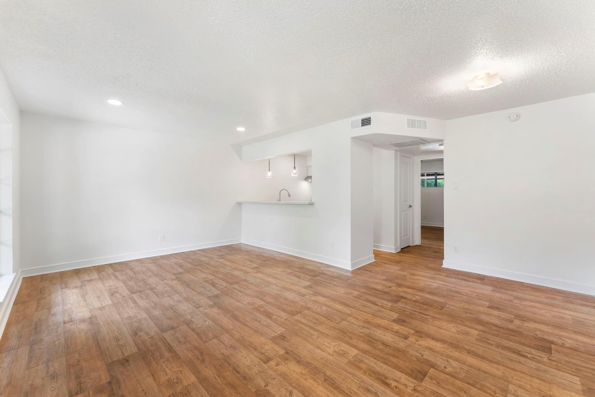 Vacant living room with wood-look floors and an open kitchen pass-through.
