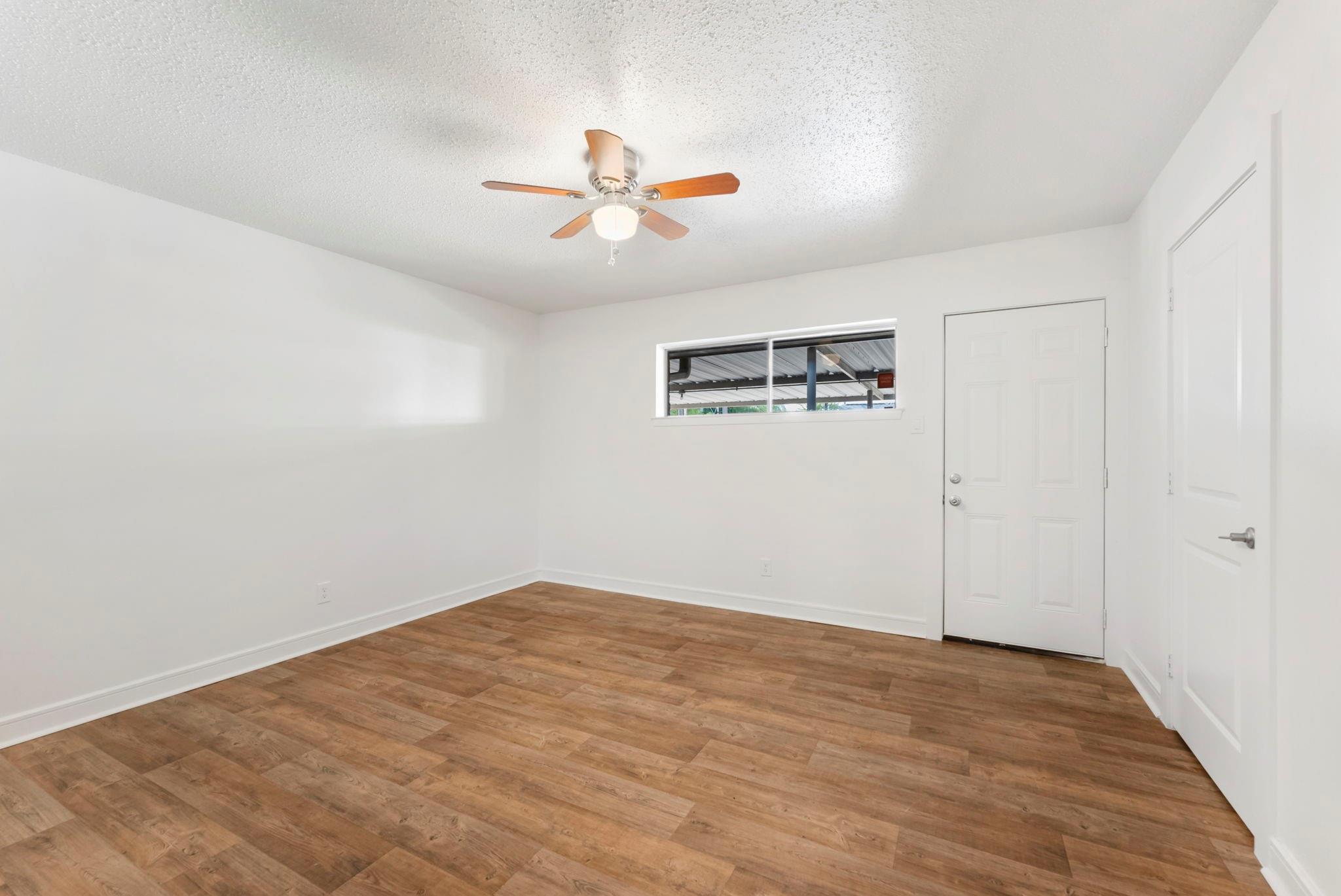 Empty room with wood-look flooring, a ceiling fan, a narrow window, and two white doors.