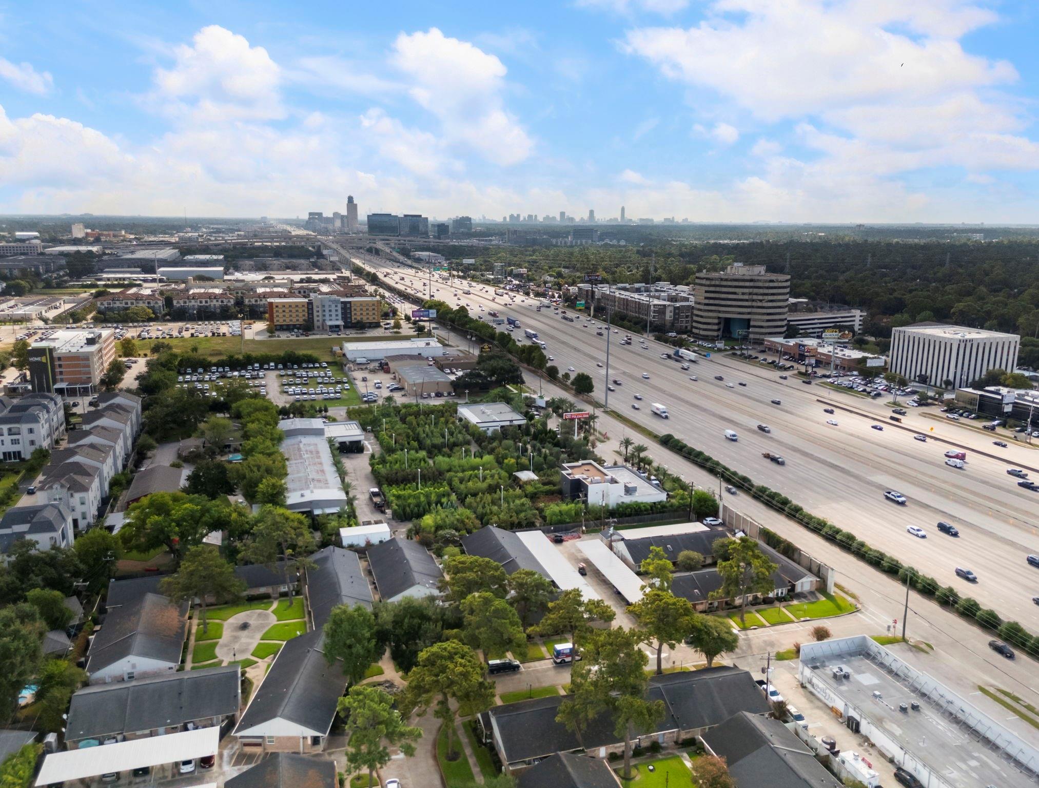 Aerial neighborhood beside a busy highway, with a distant city skyline.