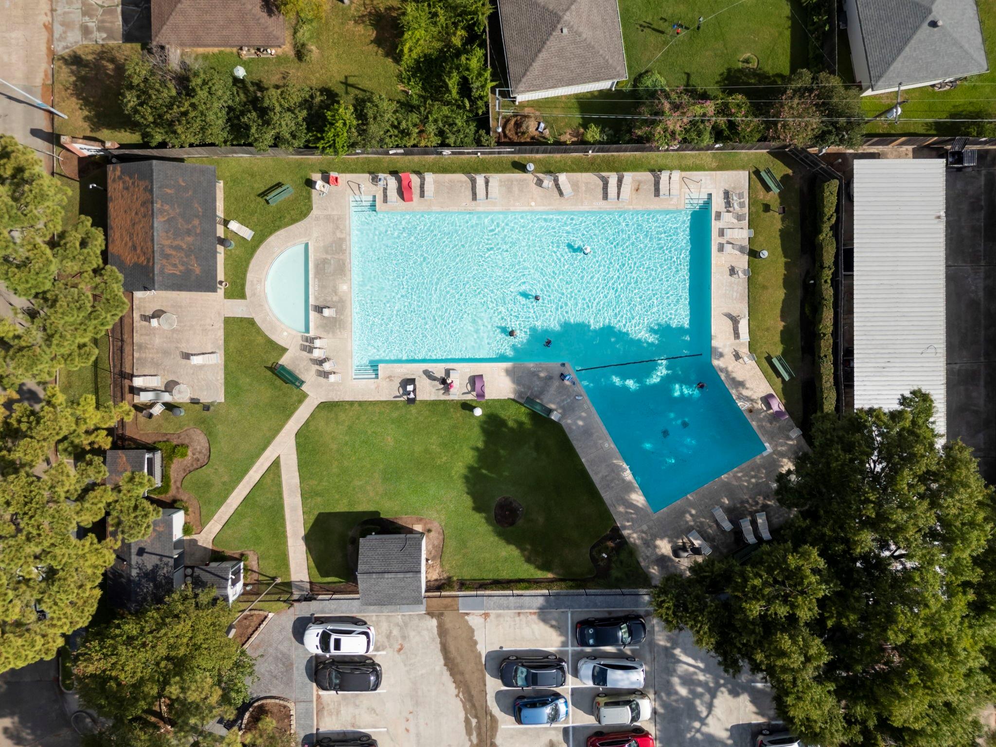 Aerial view of a community pool with a separate wading pool, lounge chairs, and landscaped grounds.