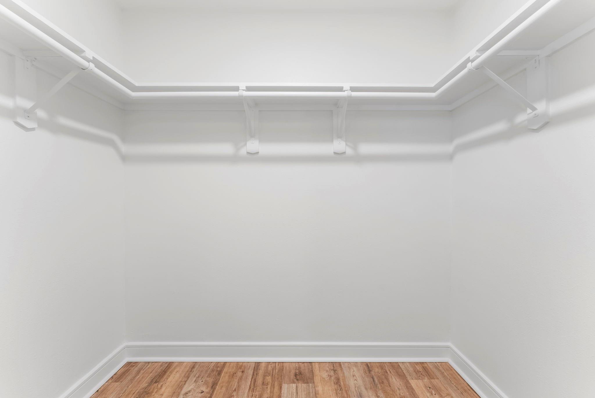 Empty closet with an upper hanging rod and shelf above a wood-look floor.