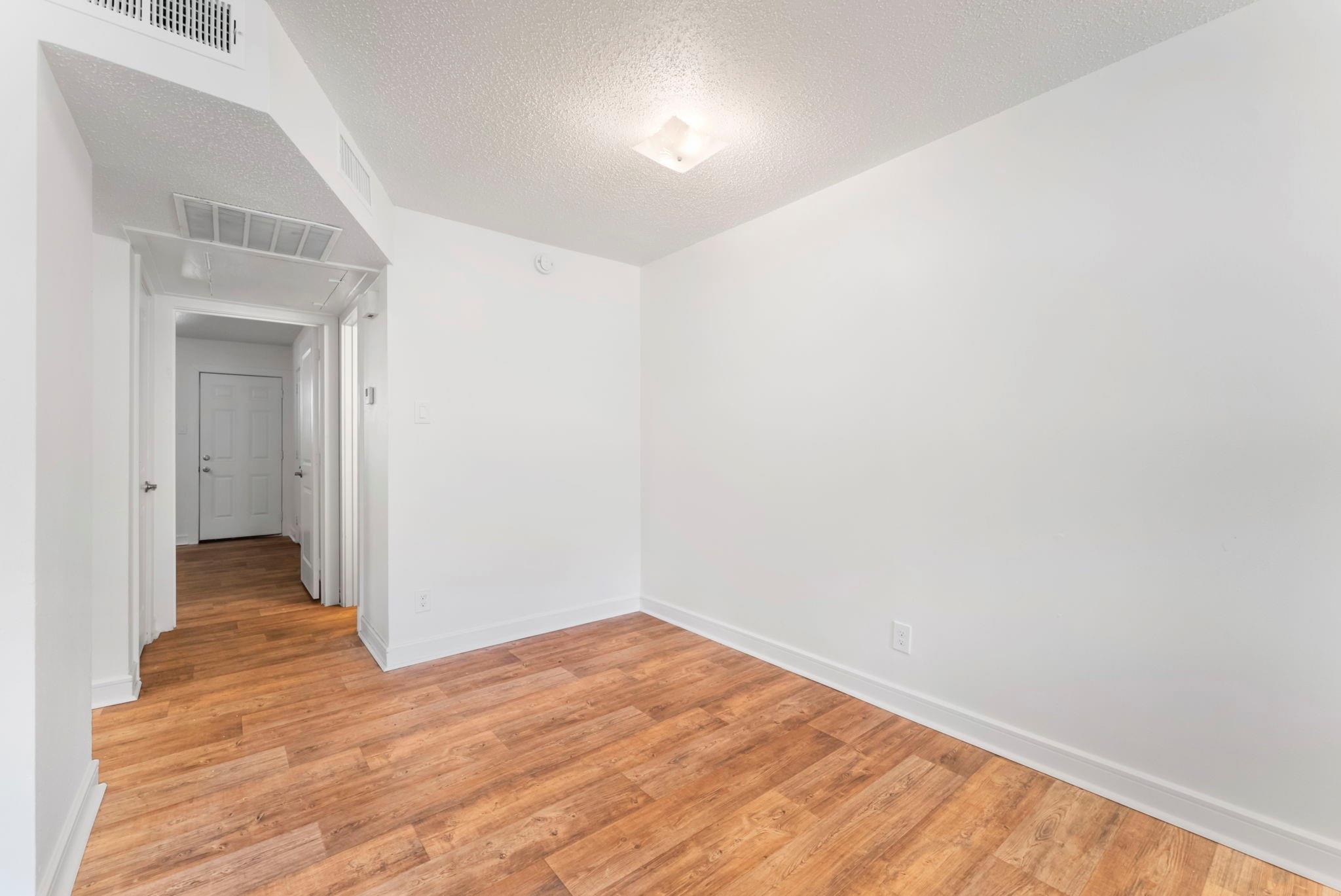 Vacant room with warm hardwood floors and a hallway leading to the front door.