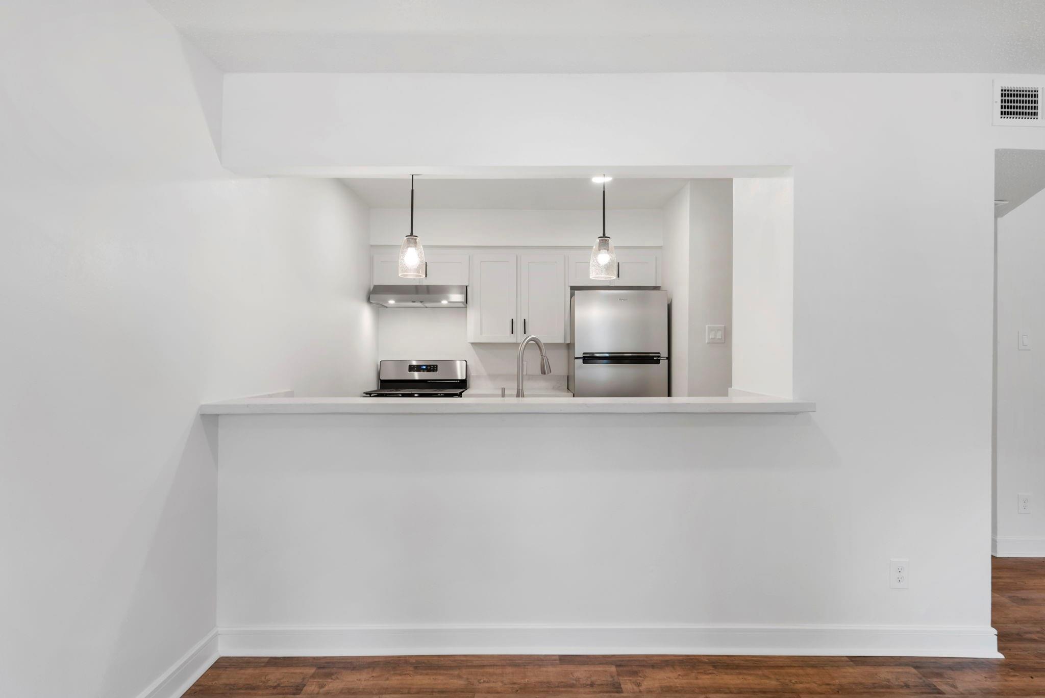White kitchen with a wide breakfast bar, stainless steel appliances, and pendant lights.
