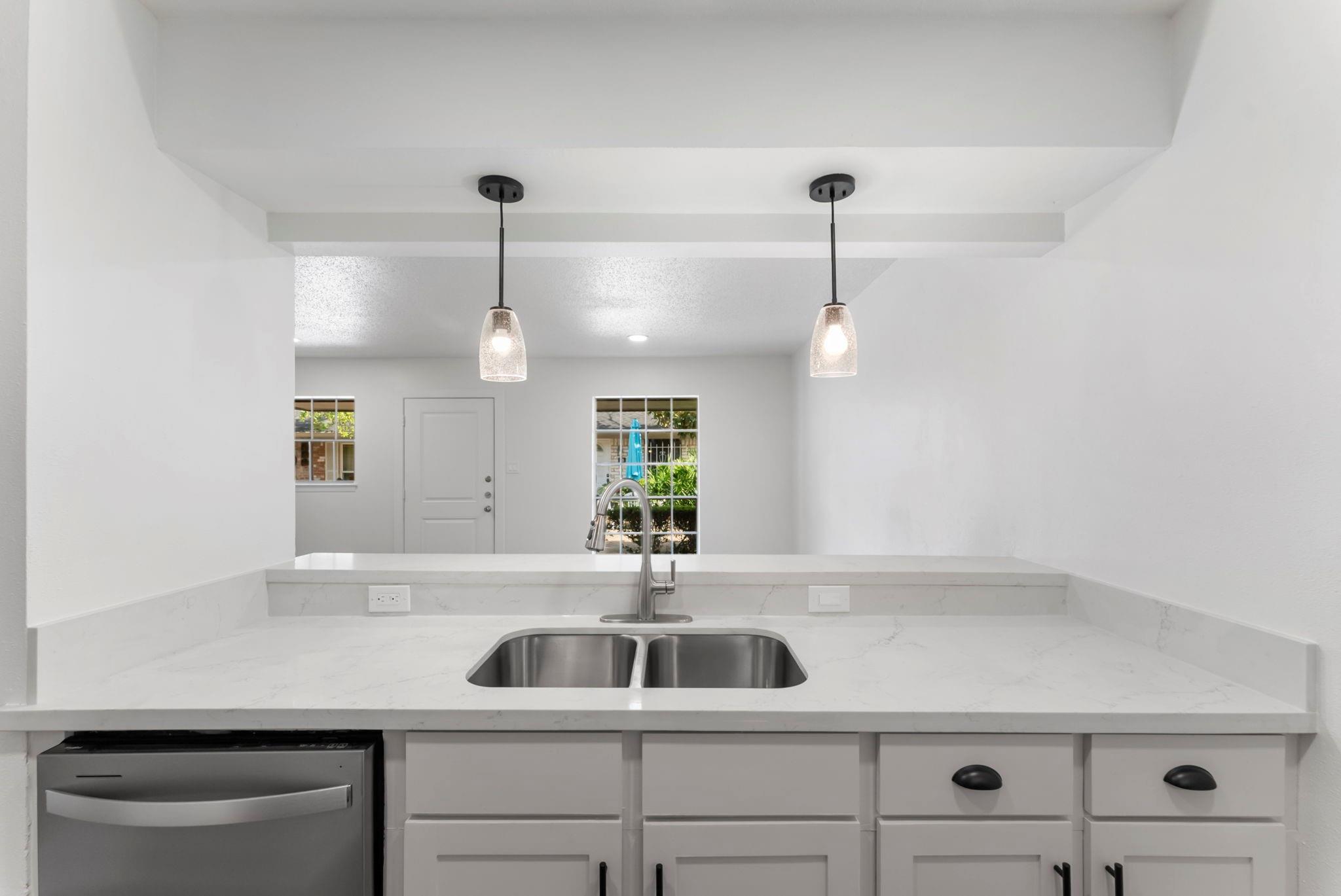 Vacant kitchen with white cabinetry, marble-look counters, a double-basin sink, and pendant lights.