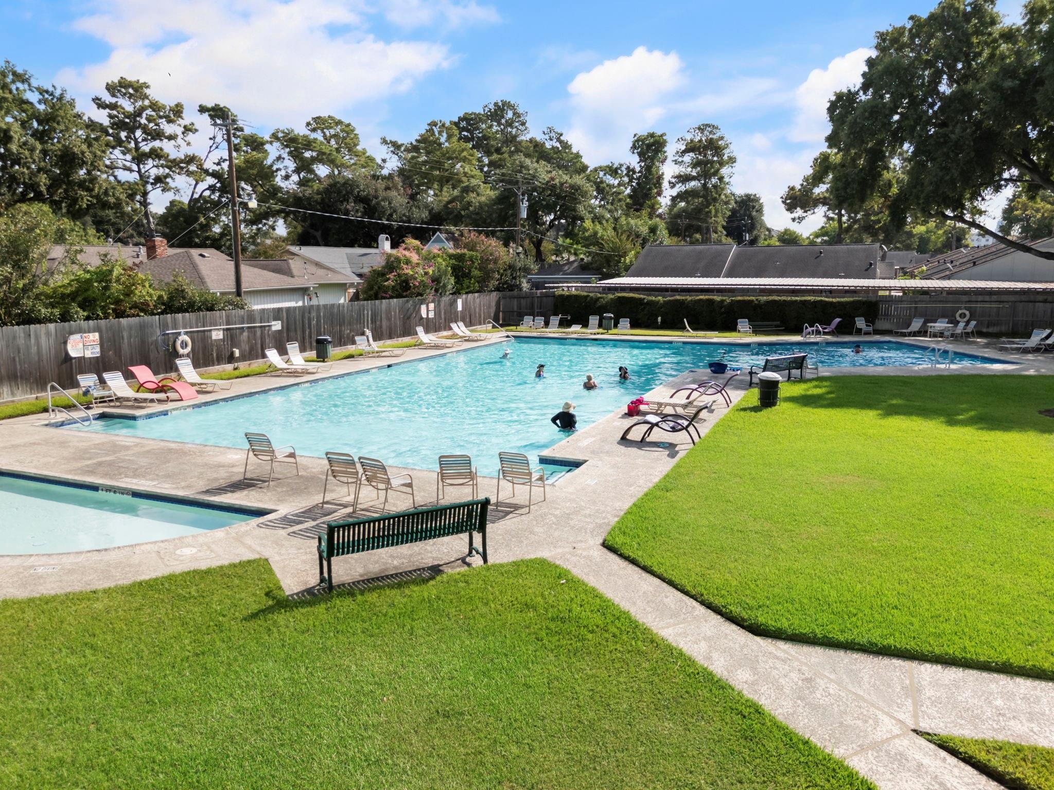Community swimming pool with swimmers, lounge chairs, and a wide lawn.