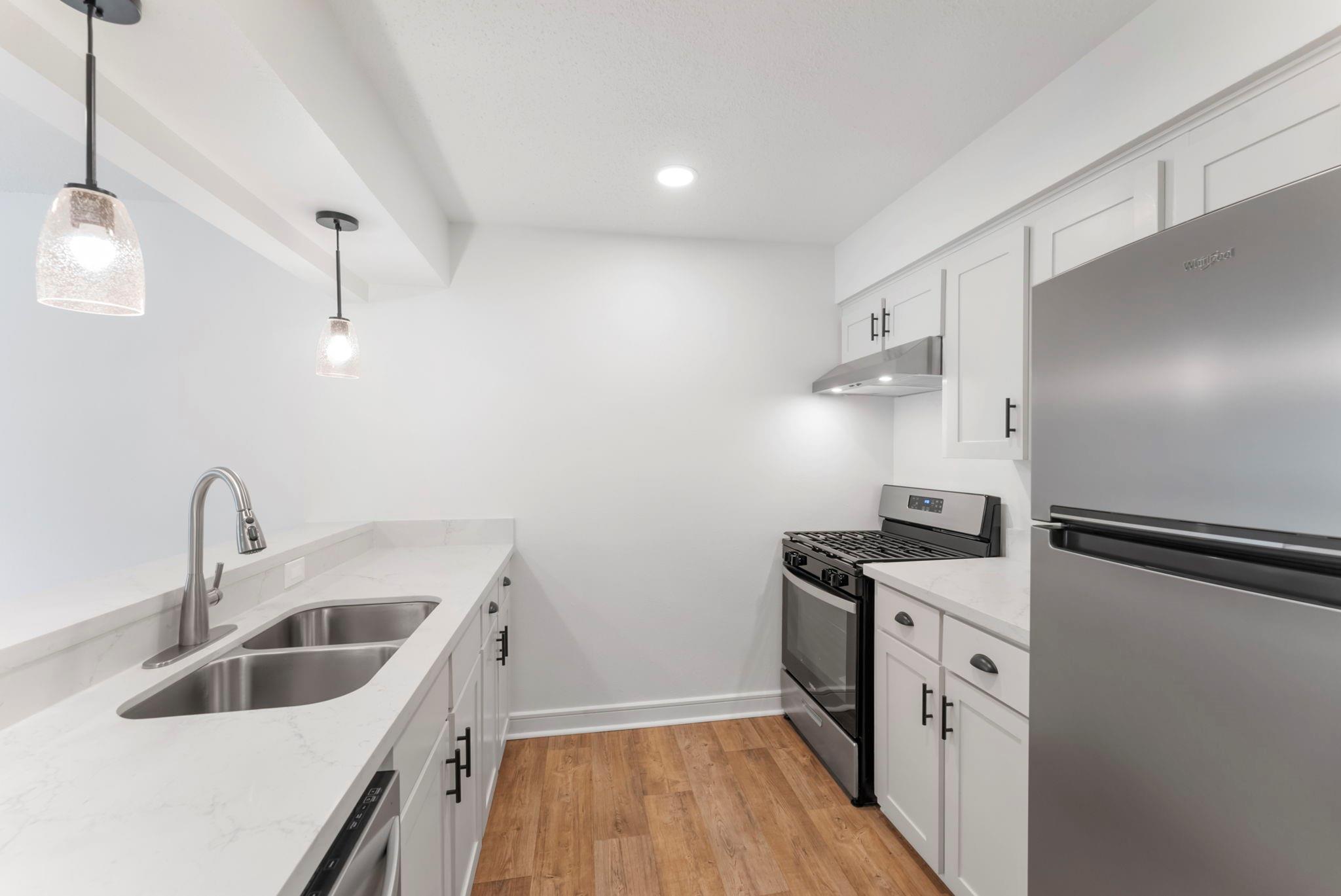 Bright white kitchen with shaker cabinets, a double-basin sink, stainless appliances, and warm wood-look flooring.