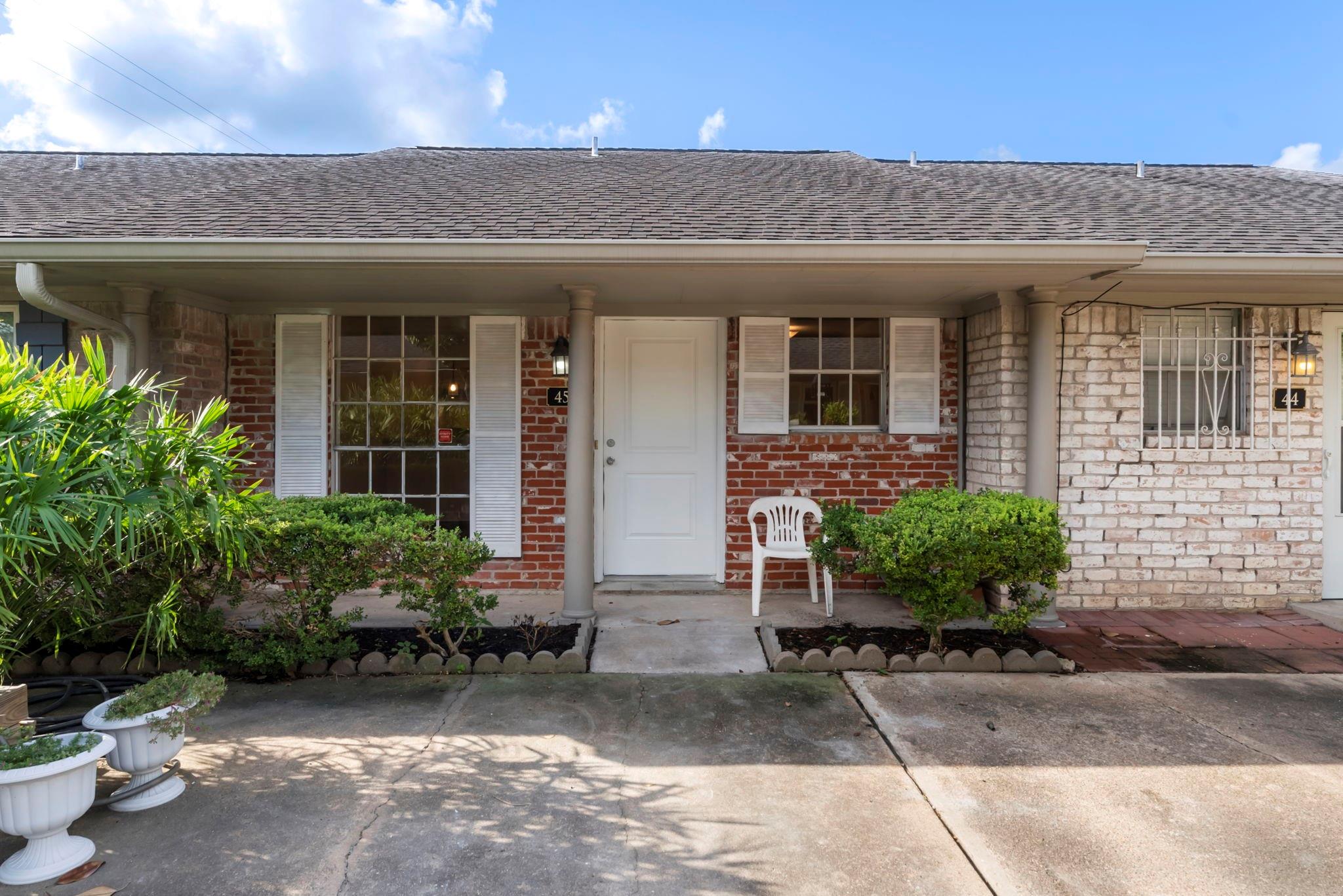 Brick home exterior with a covered entry, white door, and landscaped front beds.