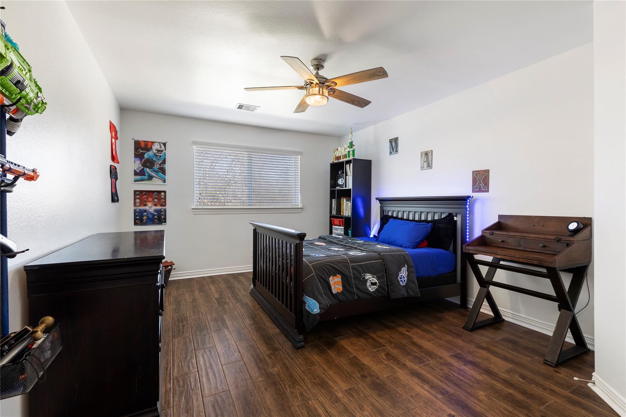 Bedroom with sports-themed bedding, a dark wooden bed, and wood-look flooring.