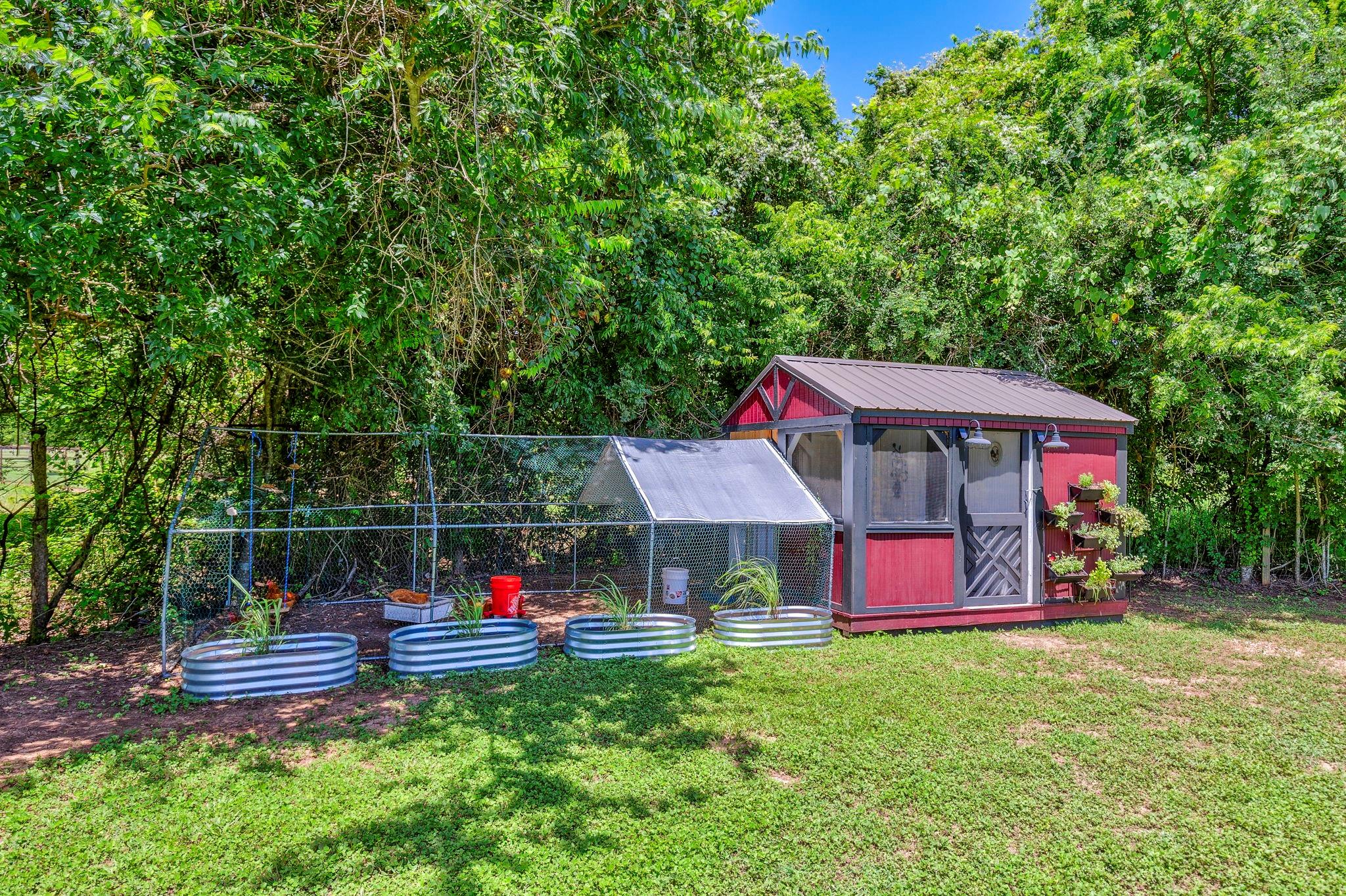 Red garden shed and screened garden enclosure beside raised beds in a wooded yard.