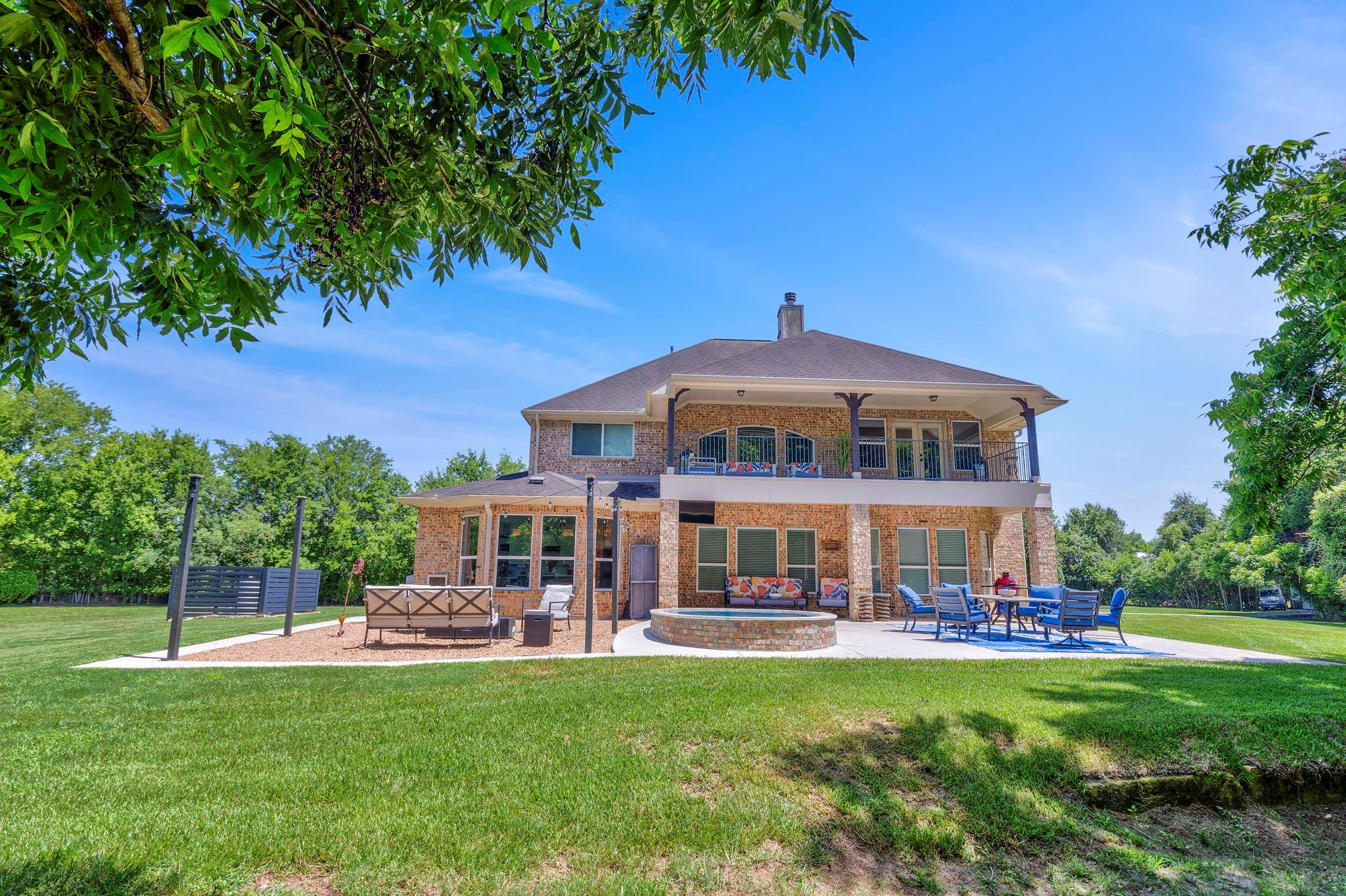 Two-story brick home with a balcony, covered patio, circular spa, and broad green lawn.