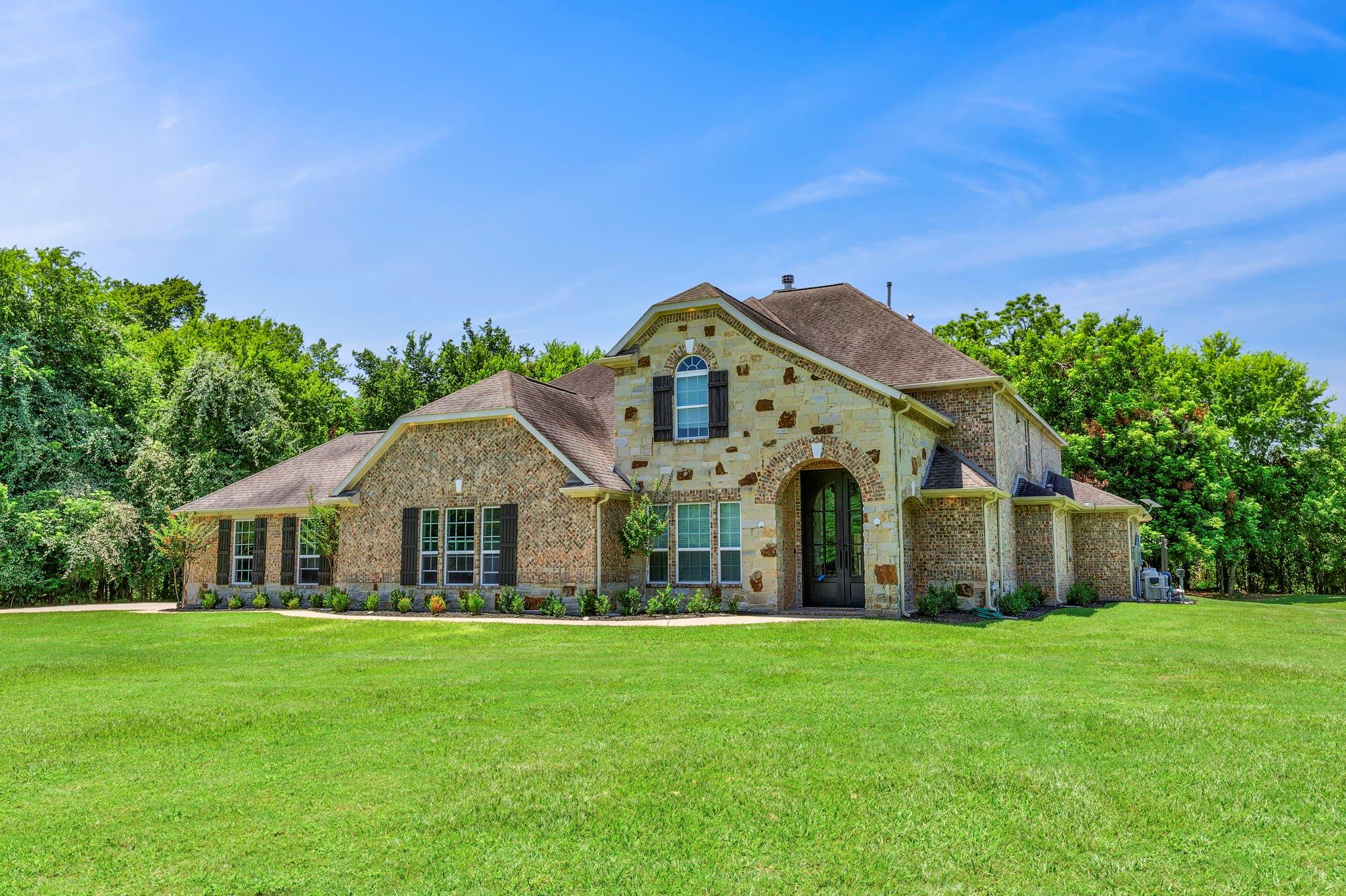Two-story stone-and-brick home with an arched entry, dark shutters, and a broad lawn.
