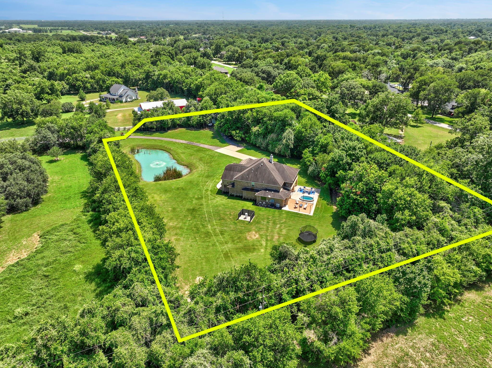 Aerial view of a wooded property with a house, swimming pool, and pond inside a yellow boundary.