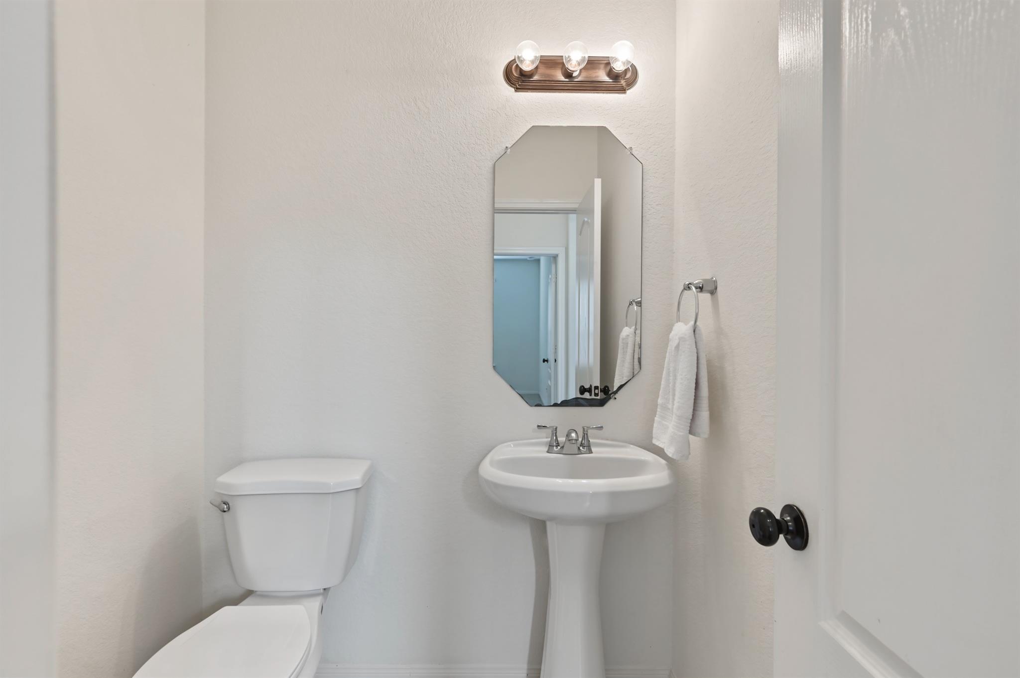 Bathroom with a pedestal sink, octagonal mirror, and toilet beside the doorway.