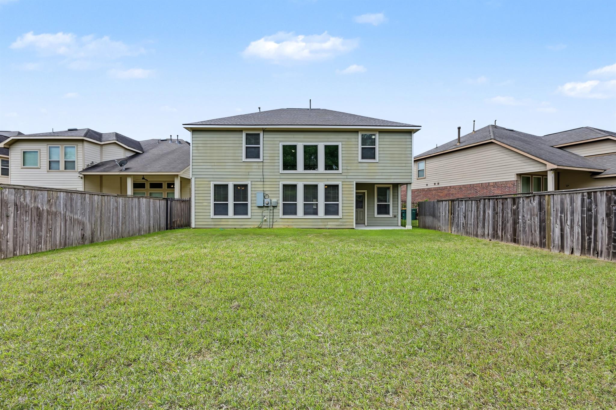 Two-story home viewed from its fenced backyard, with a broad lawn and pale green siding.