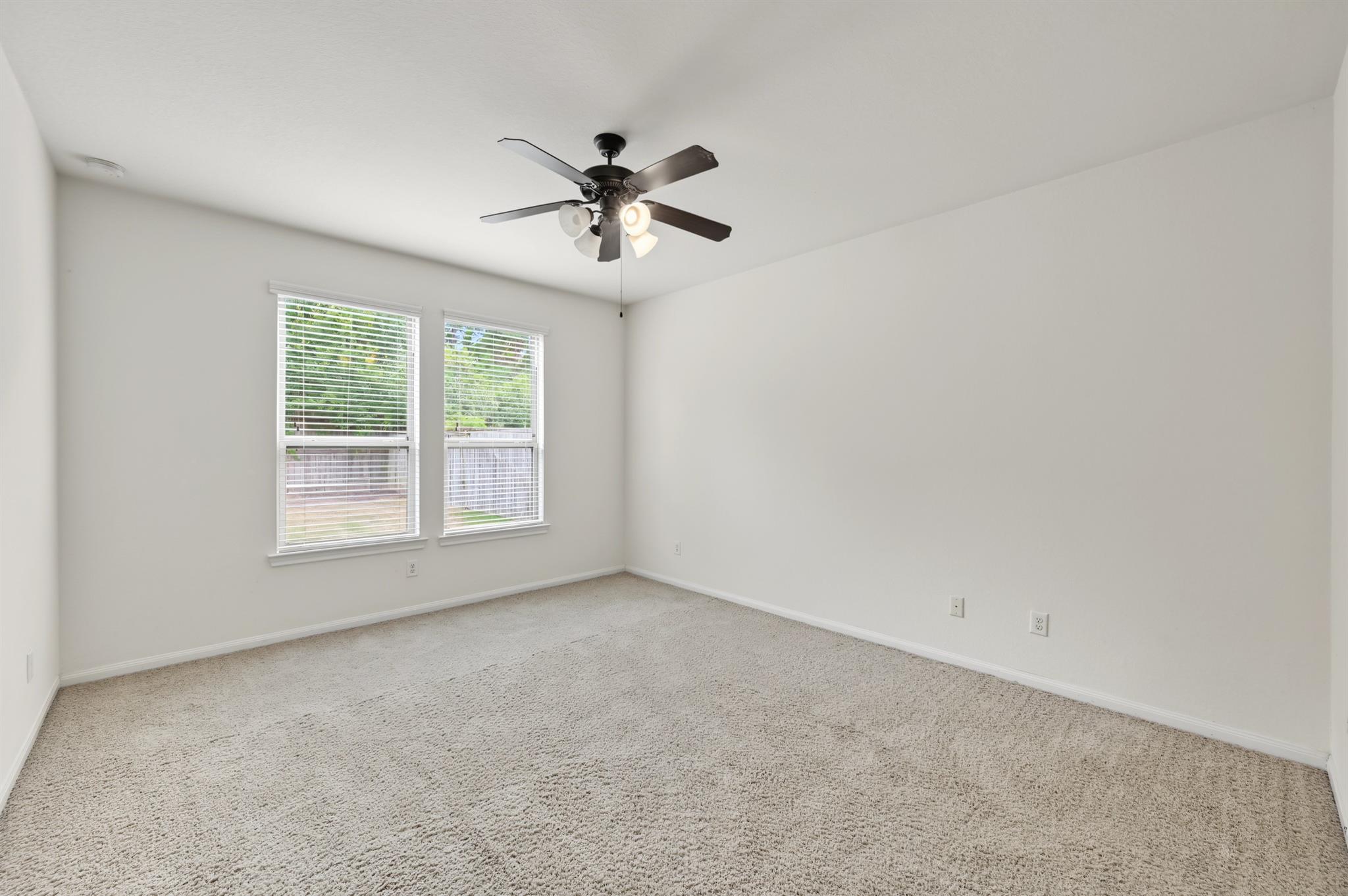 Empty bedroom with two windows and a dark ceiling fan with lights.