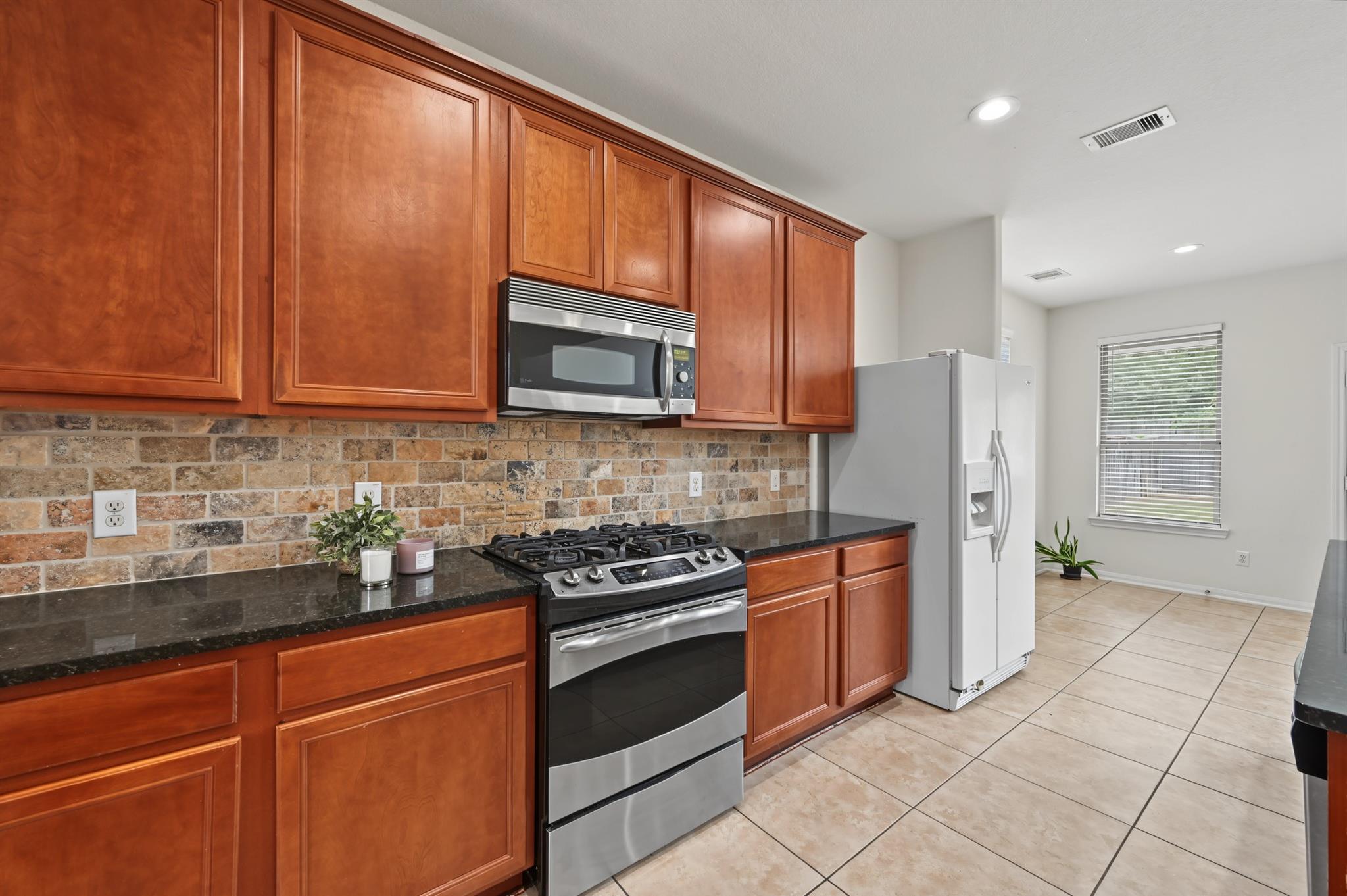 Kitchen with reddish wood cabinets, stone backsplash, and stainless steel appliances.