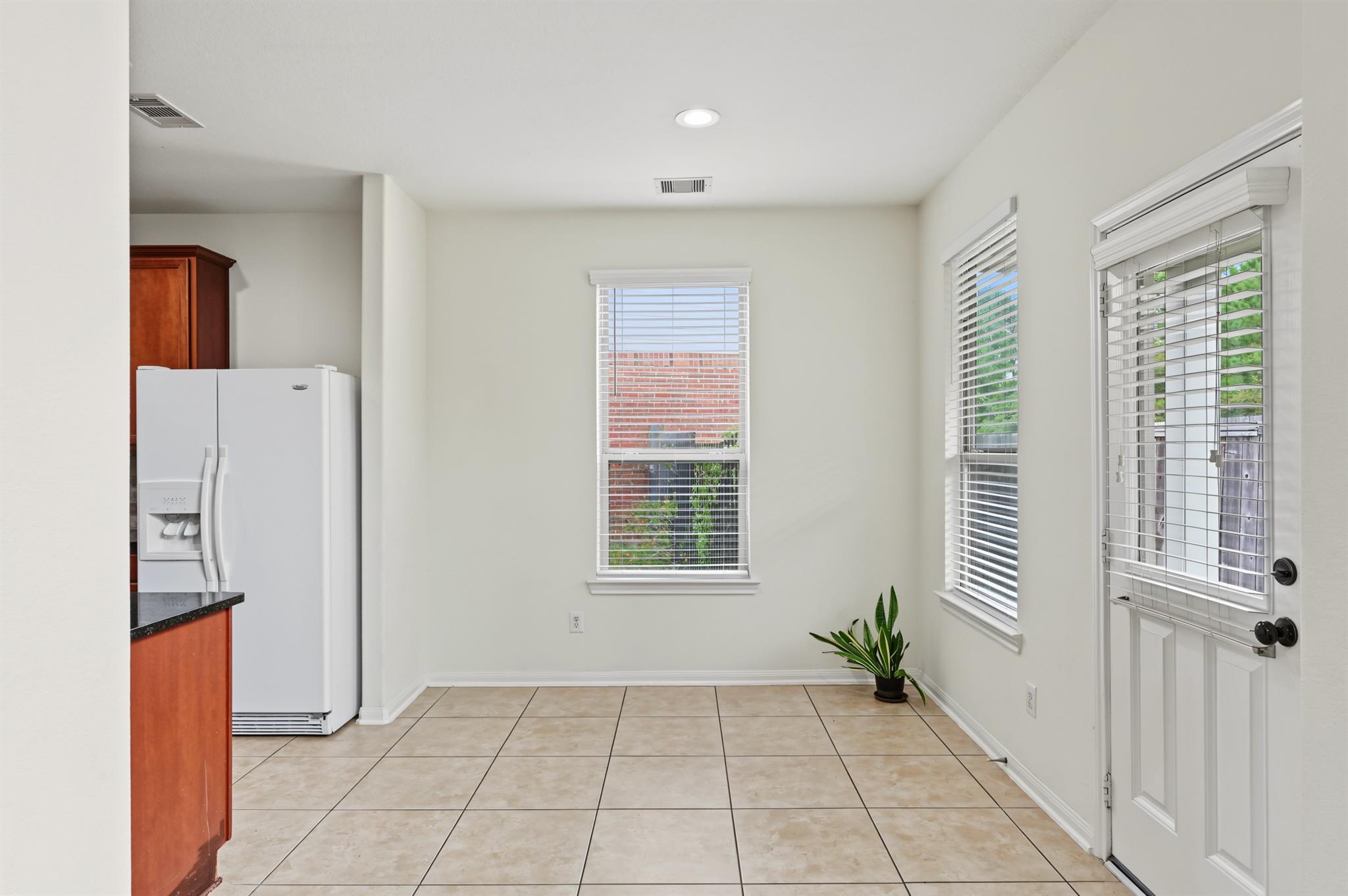 Kitchen area with tiled floors, white refrigerator, wood cabinetry, and a windowed exterior door.