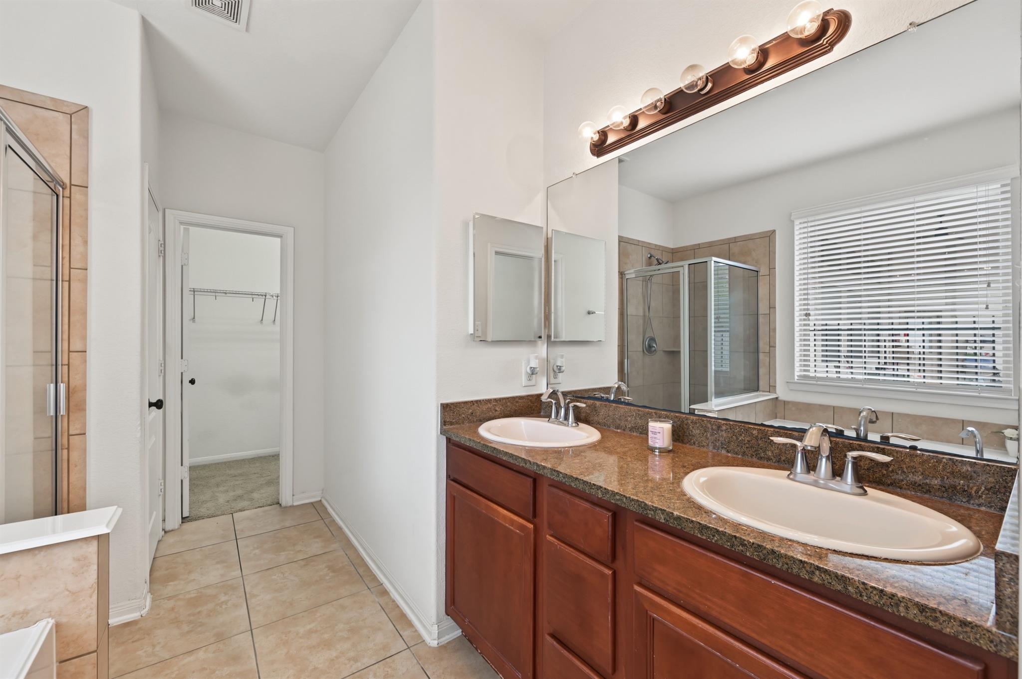 Bathroom with a double-sink vanity, granite countertop, large mirror, and glass-enclosed shower.