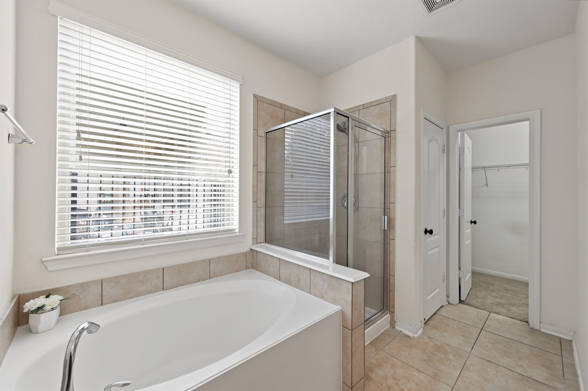 Bathroom with a large soaking tub beside a tiled glass shower and wide window.