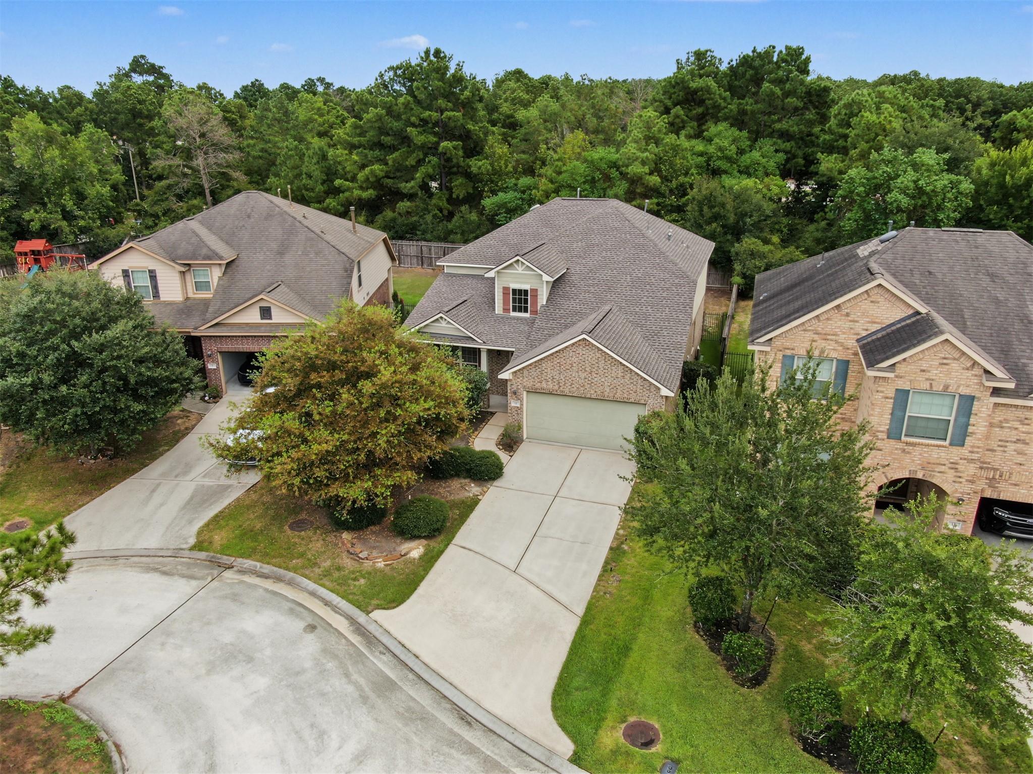 Aerial view of a brick home with a two-car garage, landscaped yard, and mature trees.
